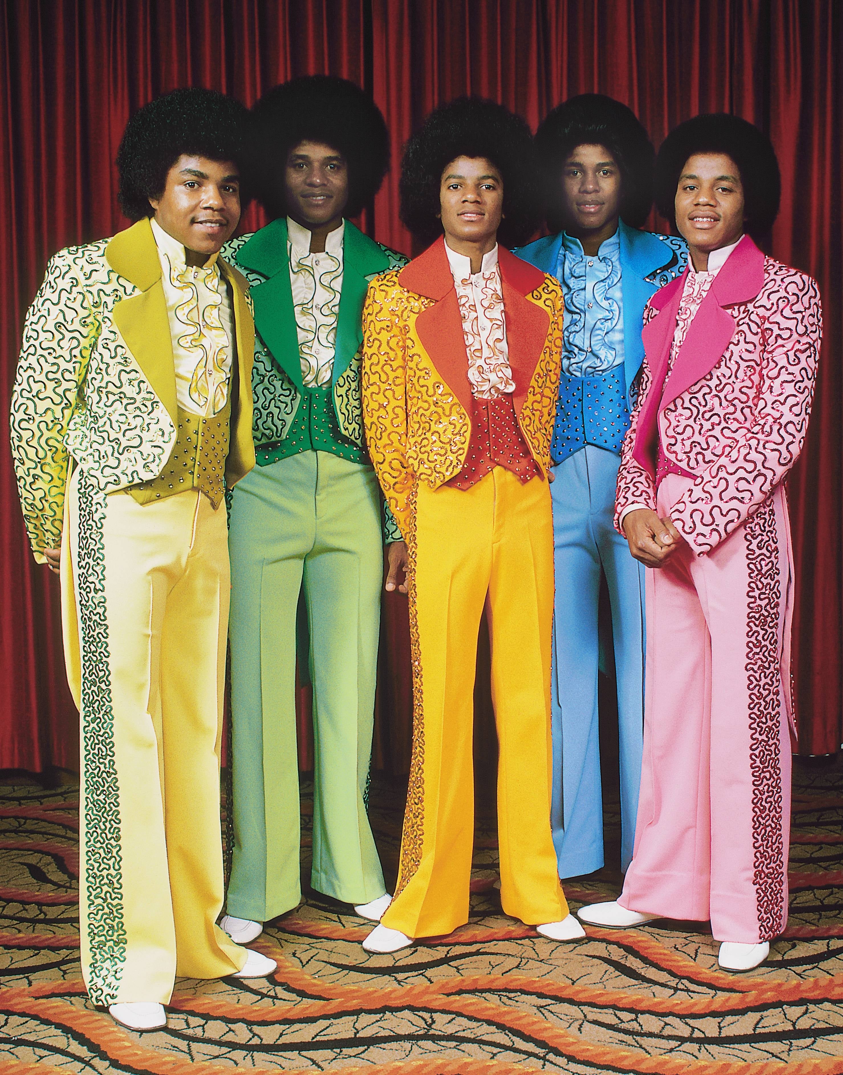 Five individuals wearing stylish, brightly colored 1970s suits with ruffled shirts, lasting  successful  beforehand   of a curtain