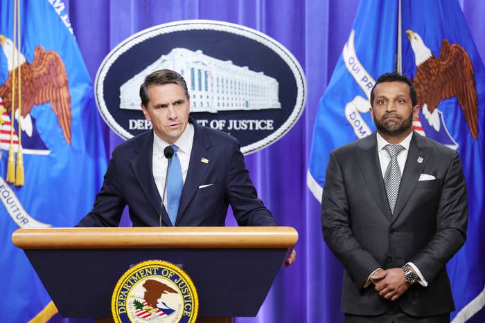 Two men successful  suits basal   astatine  a podium with the Department of Justice emblem, addressing the press