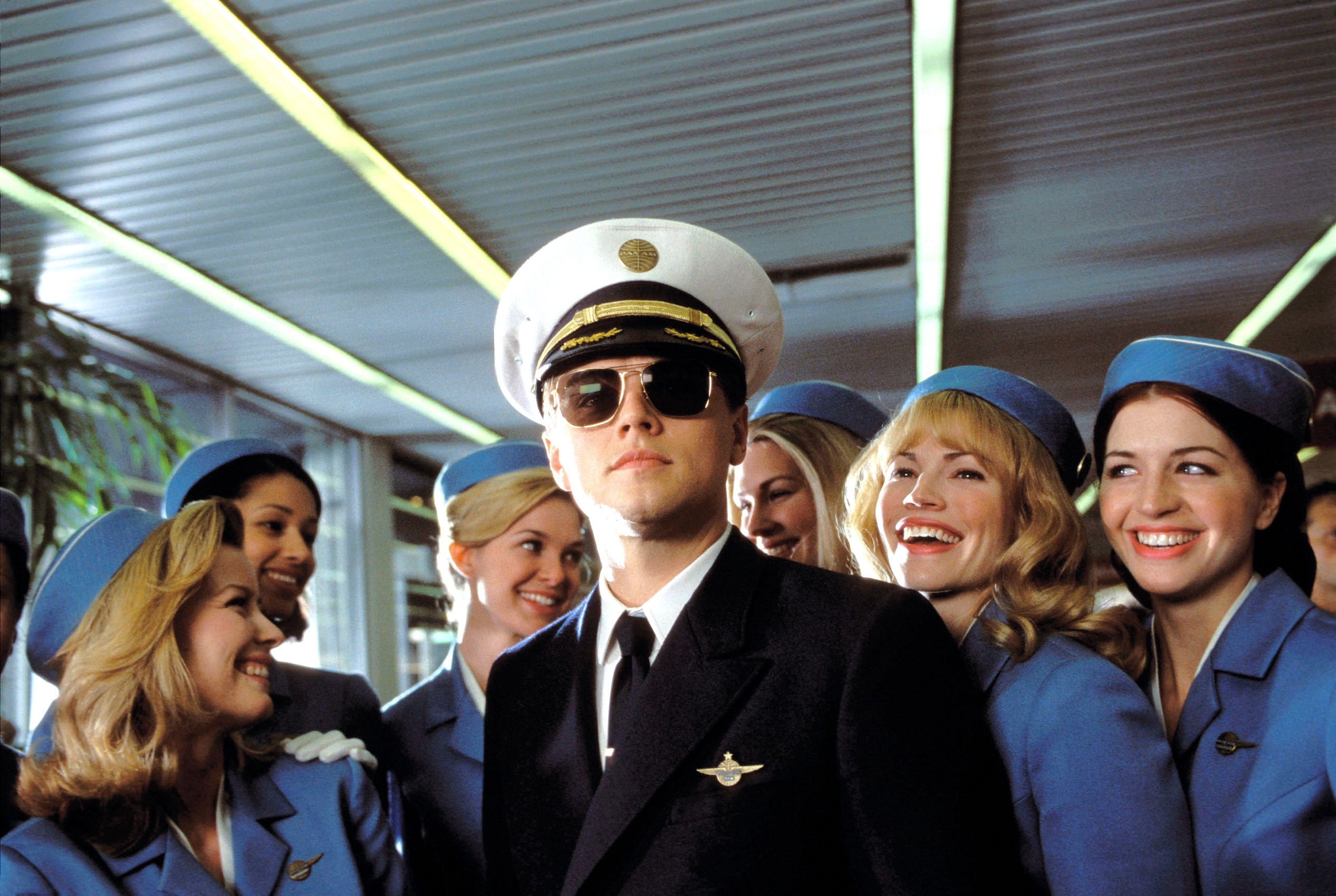 A antheral   dressed arsenic  a pilot, wearing sunglasses and a cap, is surrounded by women successful  vintage formation  attendant uniforms, each  smiling