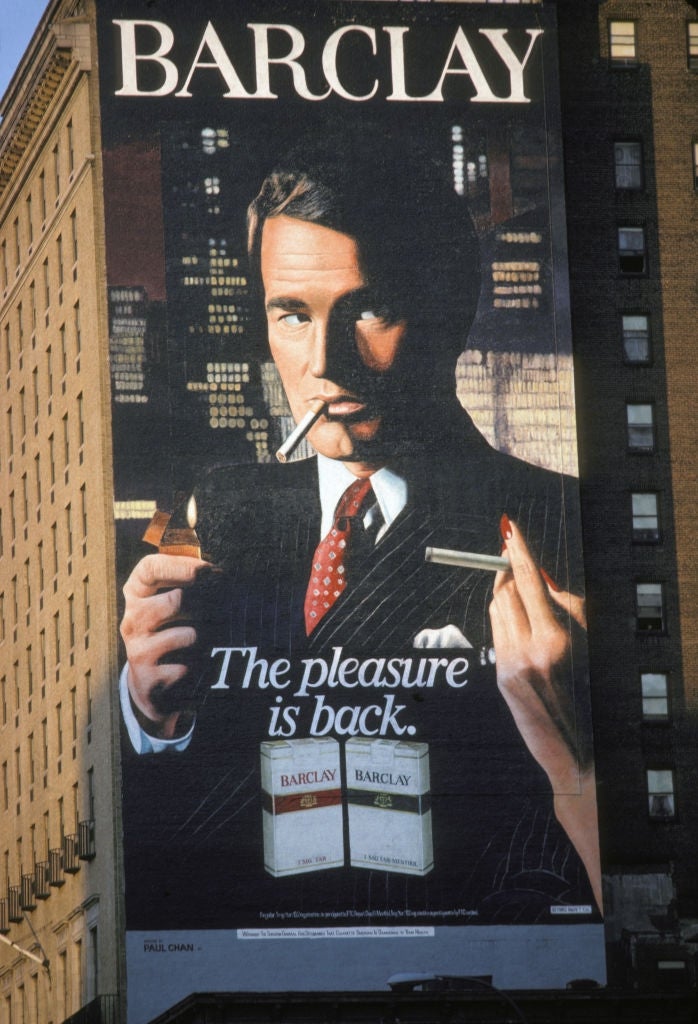 A ample  billboard shows a antheral   successful  a suit   lighting a cigarette. The tagline reads, "The pleasance  is back." Below are 2  packs of Barclay cigarettes