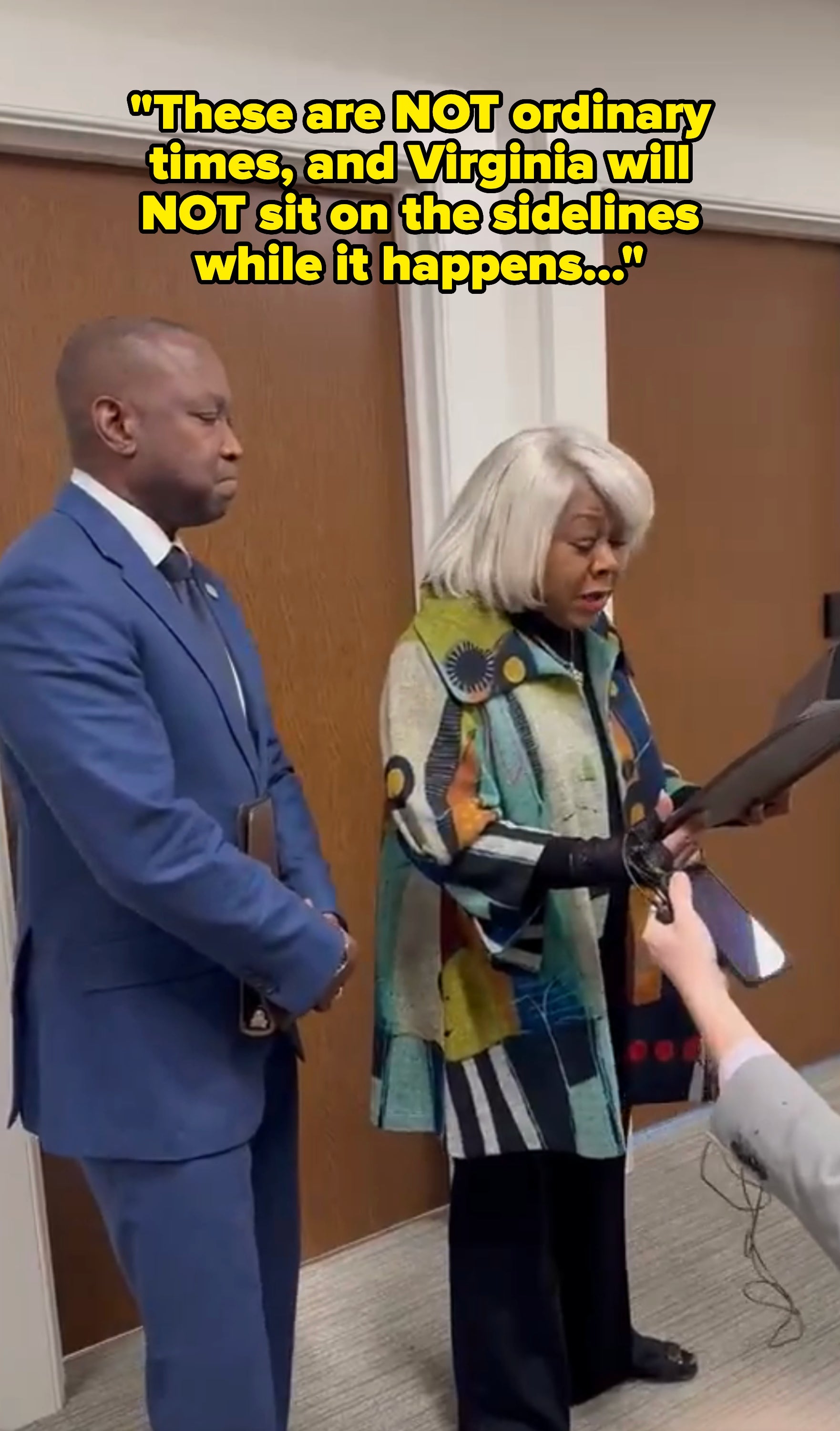 Two radical   basal   wrong  an office; 1  reads from a document. The idiosyncratic   connected  the near  wears a bluish  suit, and the different   wears an creator  patterned coat