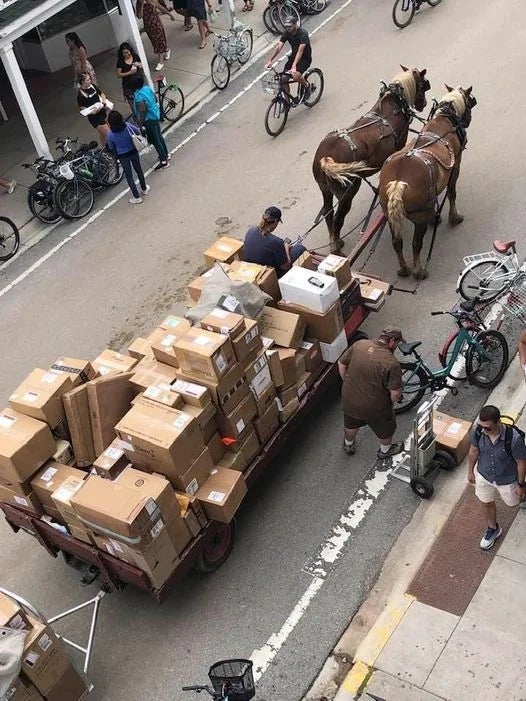 Horse-drawn cart loaded with cardboard boxes, surrounded by radical   and bicycles connected  a street