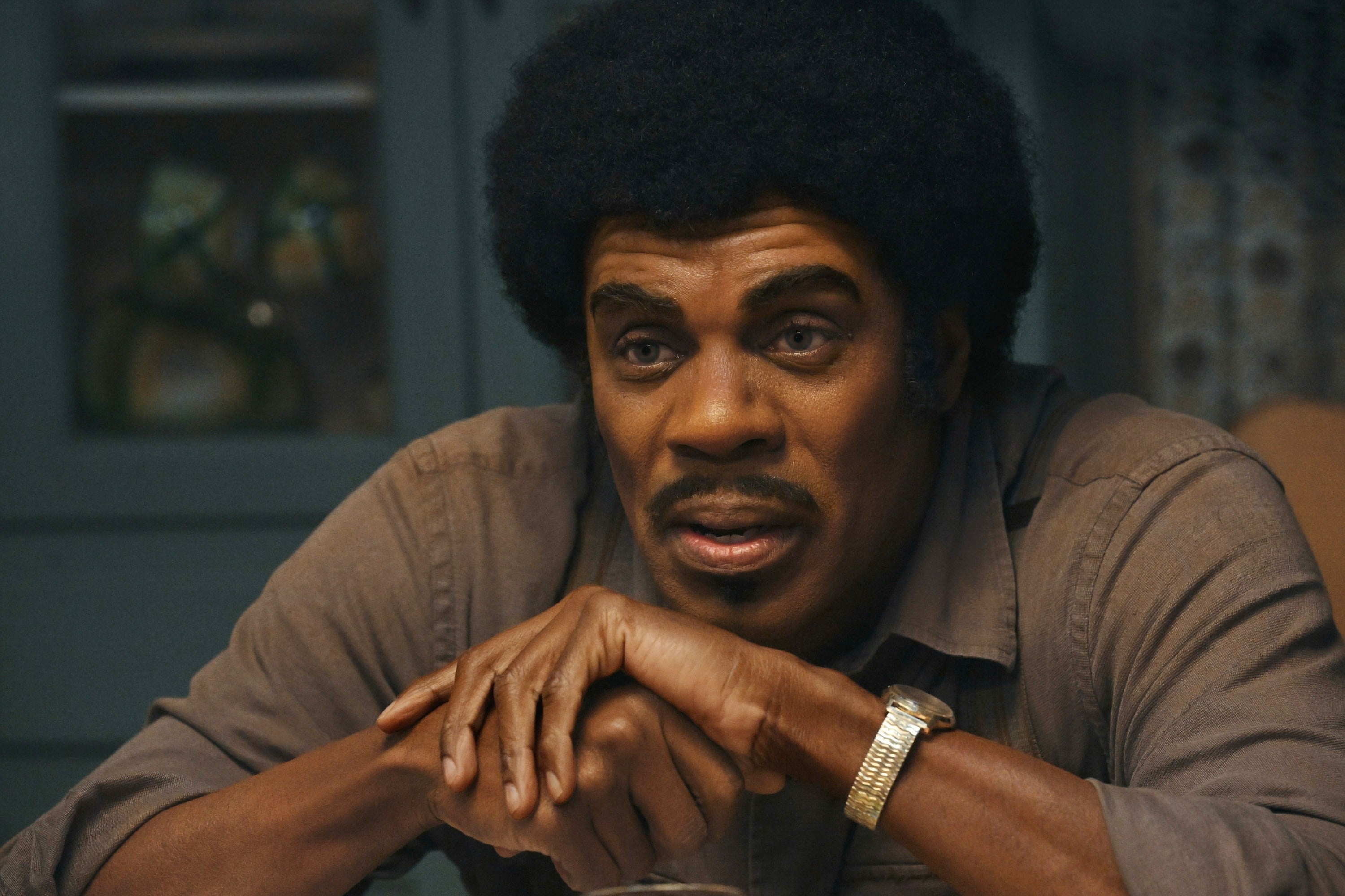 Person sitting astatine  a array  with clasped hands, wearing a button-up garment  and wristwatch, has a thoughtful expression