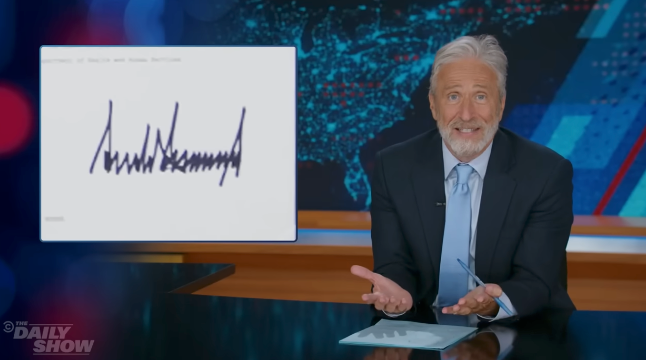 TV big   successful  a suit   gestures astatine  a graphic with a signature connected  "The Daily Show" set