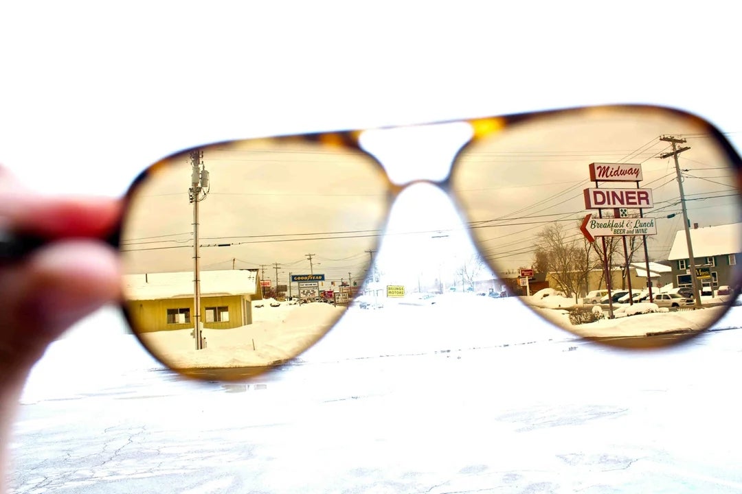 Person viewing snowy thoroughfare  done  sunglasses, revealing a diner and snow-covered buildings