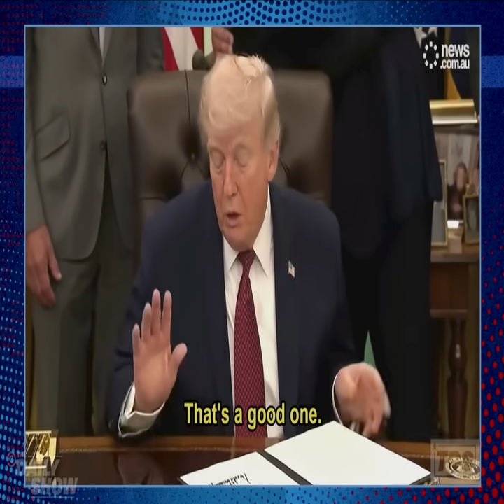 Person in a suit seated at a desk, gesturing, with subtitle: "That's a good one." Surrounded by others, appears to be at a formal event