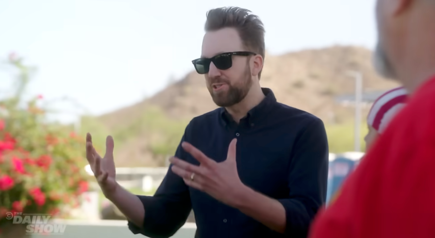 A idiosyncratic   wearing sunglasses gestures portion    speaking outdoors