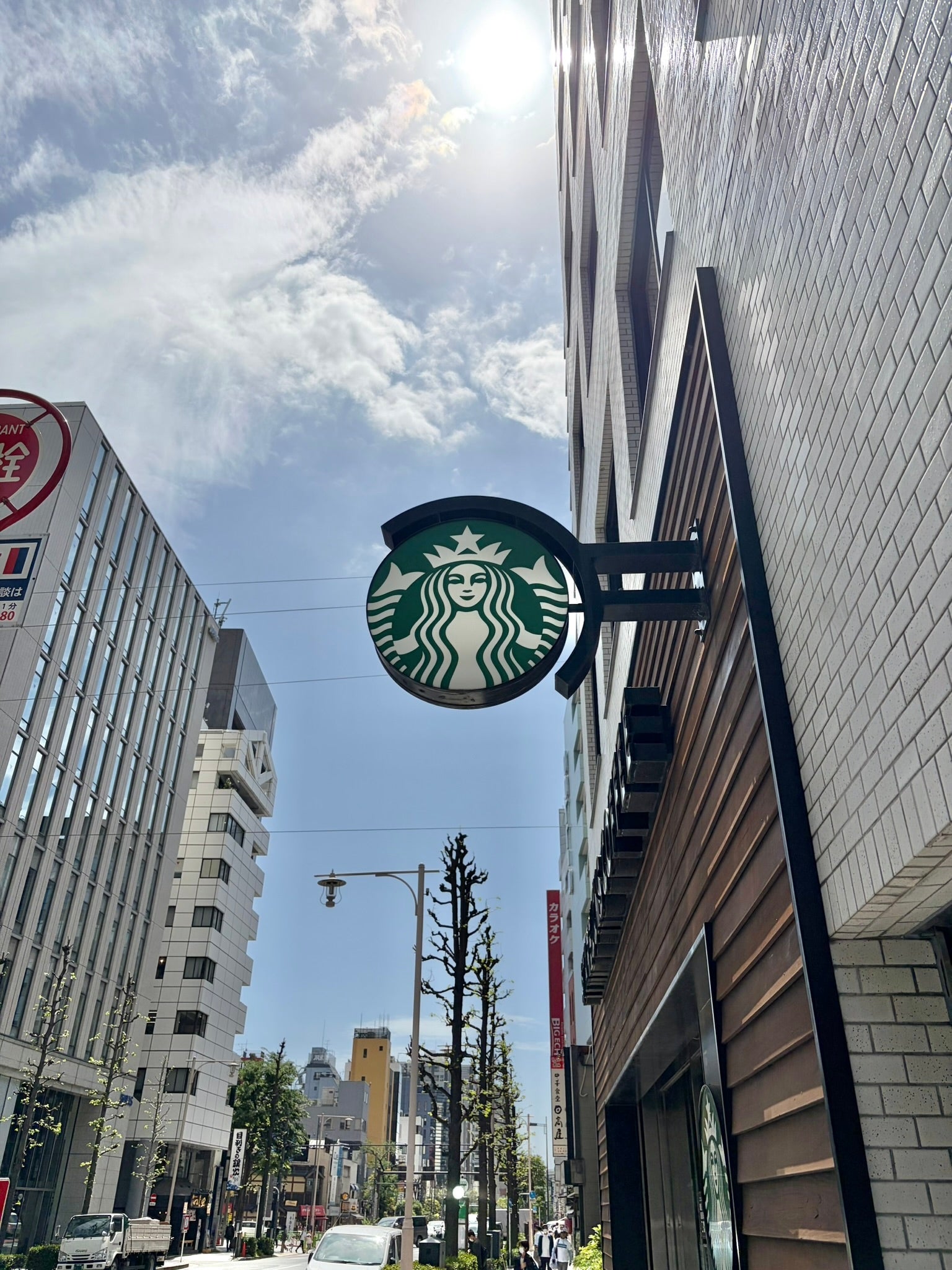 スターバックスの看板がビルの外壁に掛かっている。背景に青空と他のビルの外観が見える都市の風景。