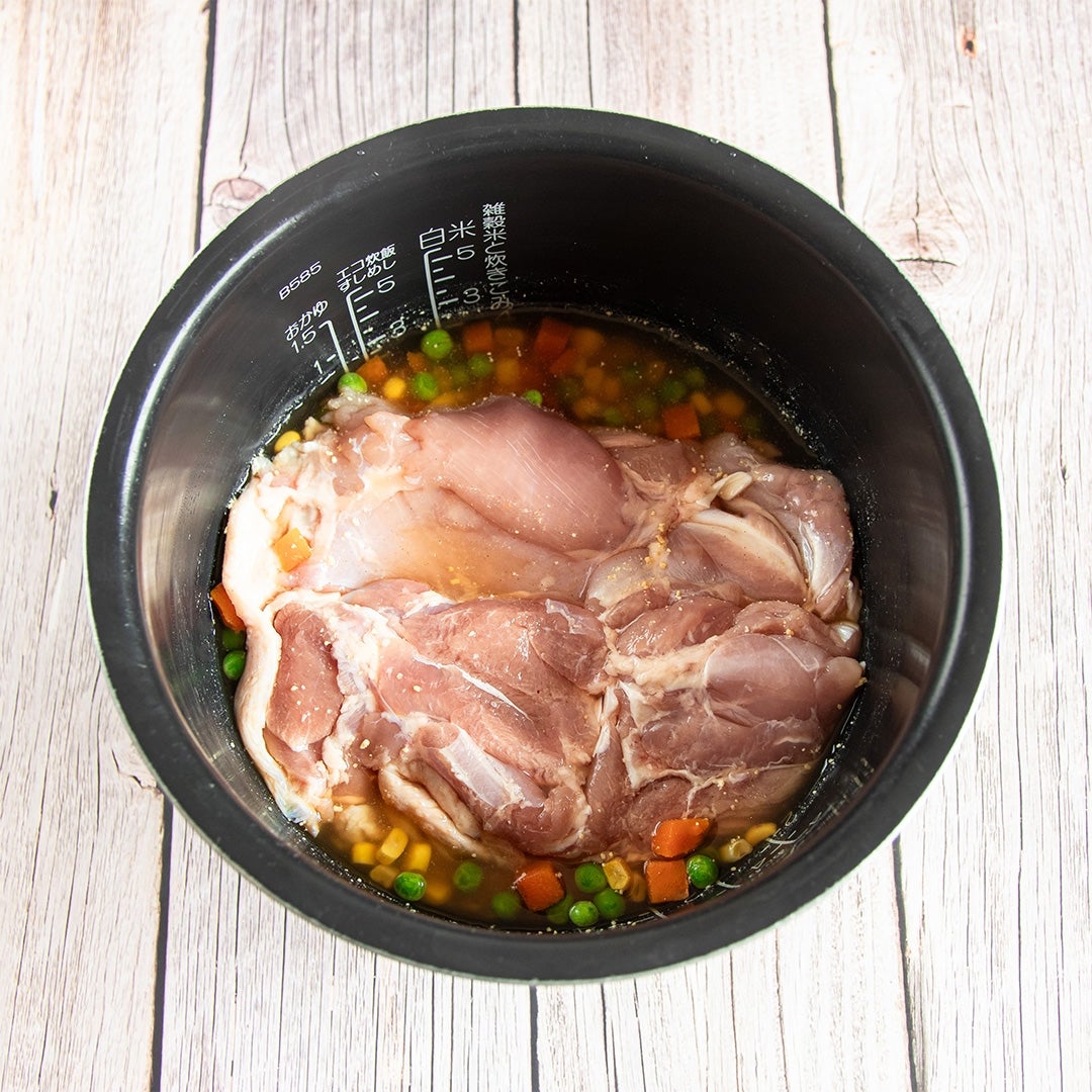 調理前の鶏肉と野菜が炊飯器に入っている。調味液に漬け込まれた状態。