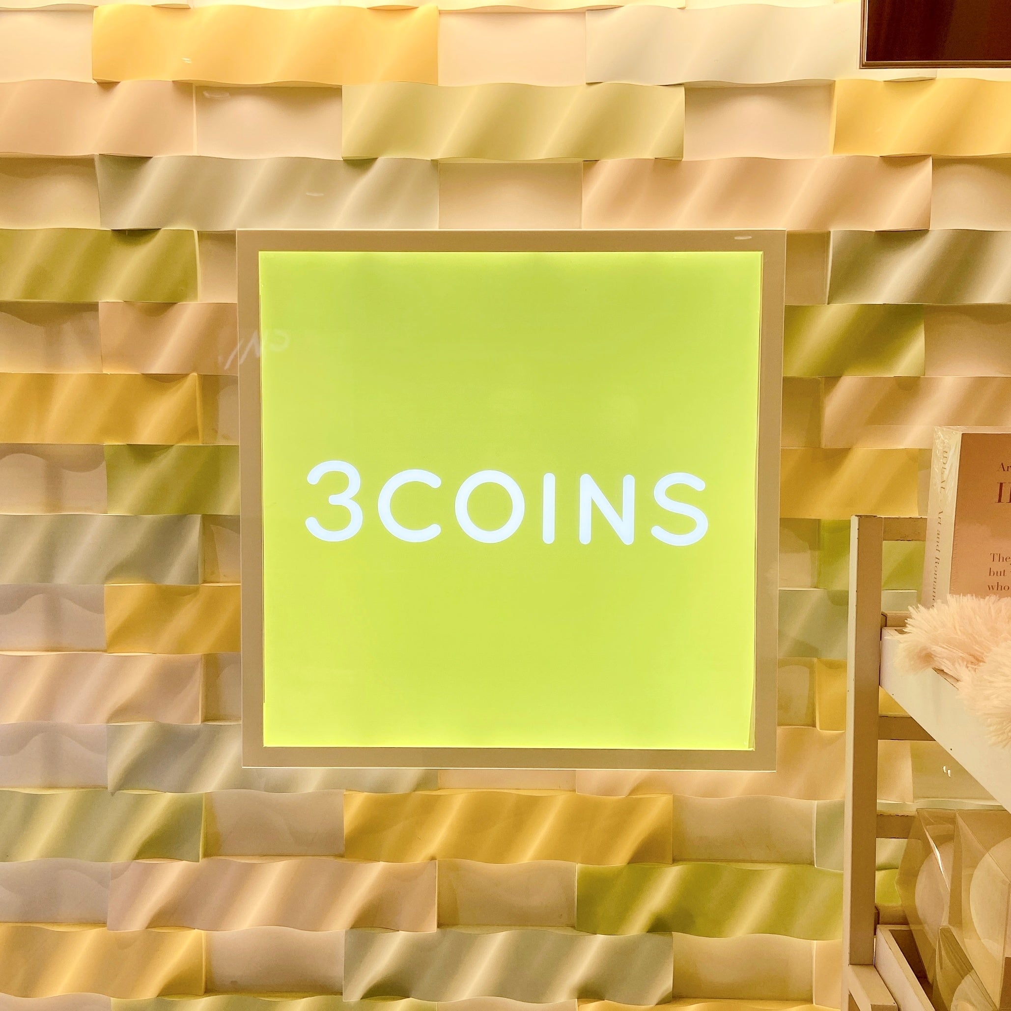 店舗の壁に「3COINS」と書かれた明るい四角い看板がある。