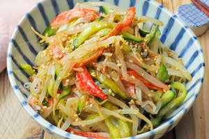 皿に盛られたもやし、カニカマ、きゅうりのサラダ。上に白ごまと調味料がかかっている。