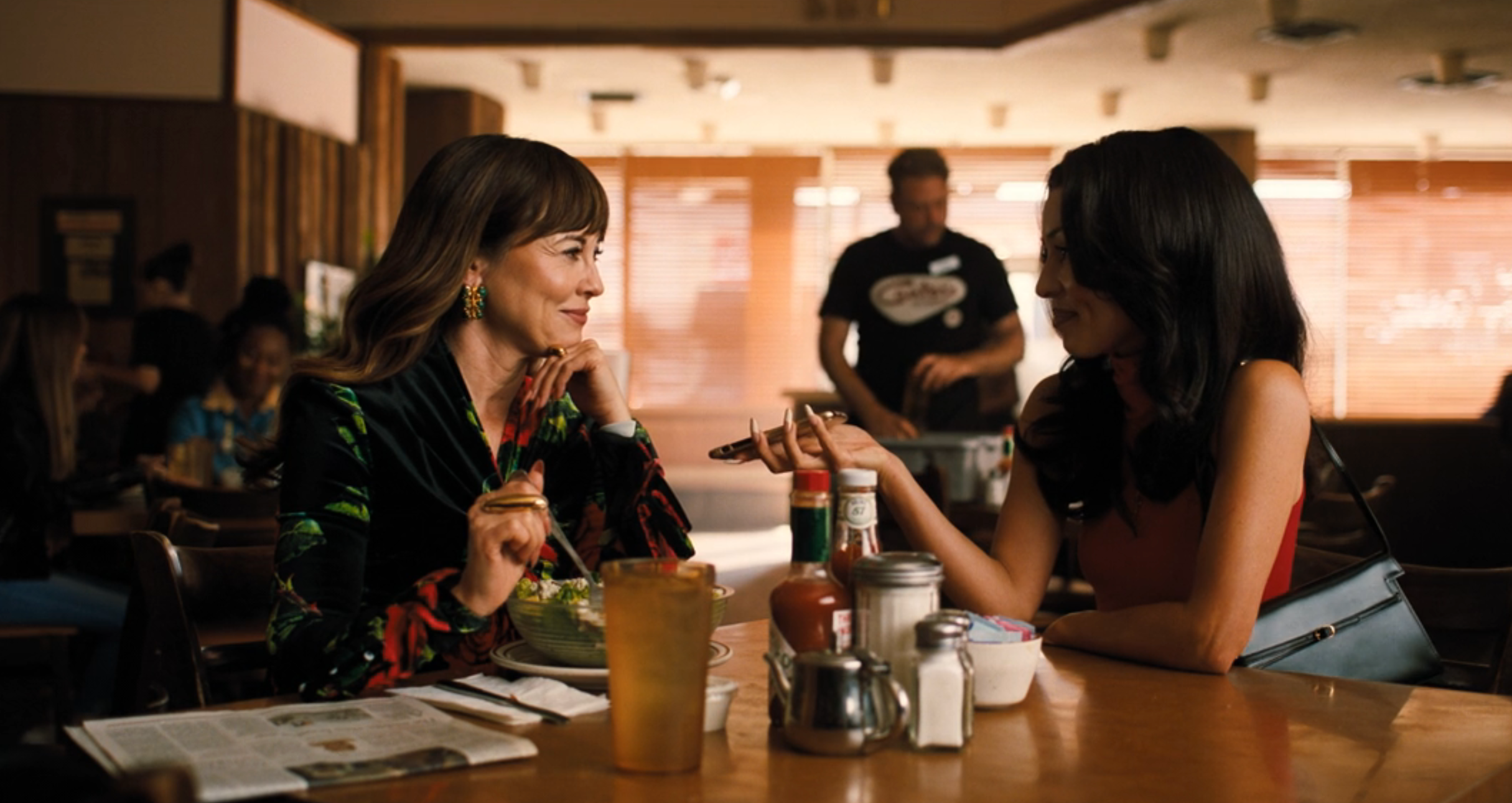 Two radical   sitting astatine  a diner table, chatting and smiling