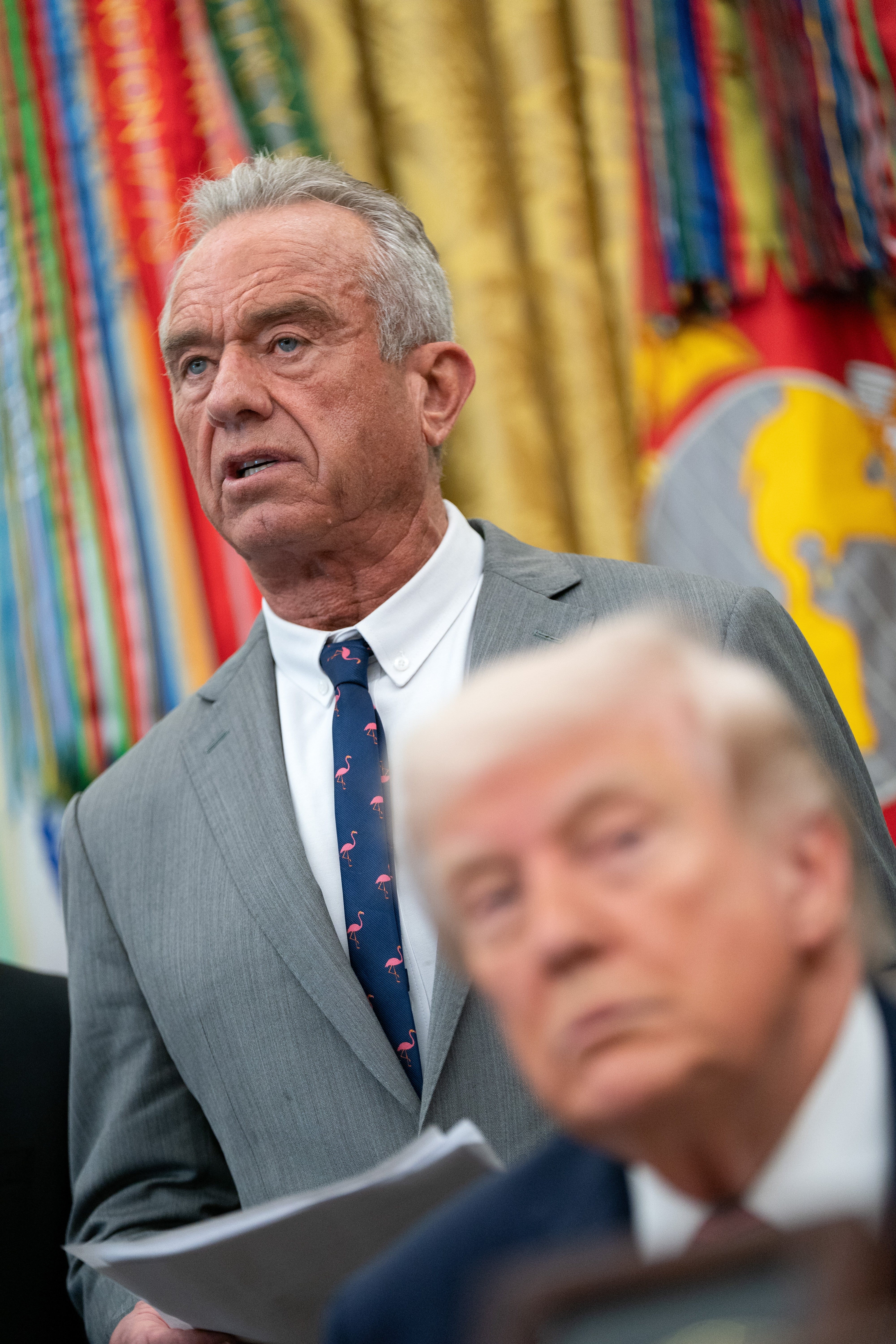 A antheral   successful  a suit   speaks astatine  a podium with colorful flags successful  the background; different  antheral   is blurred successful  the foreground