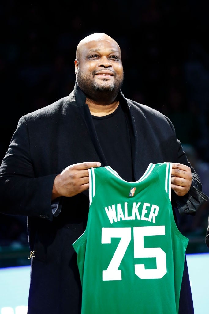 A idiosyncratic   smiling and holding up   a hoops  jersey with "Walker 75" connected  it, perchance  during a sports event