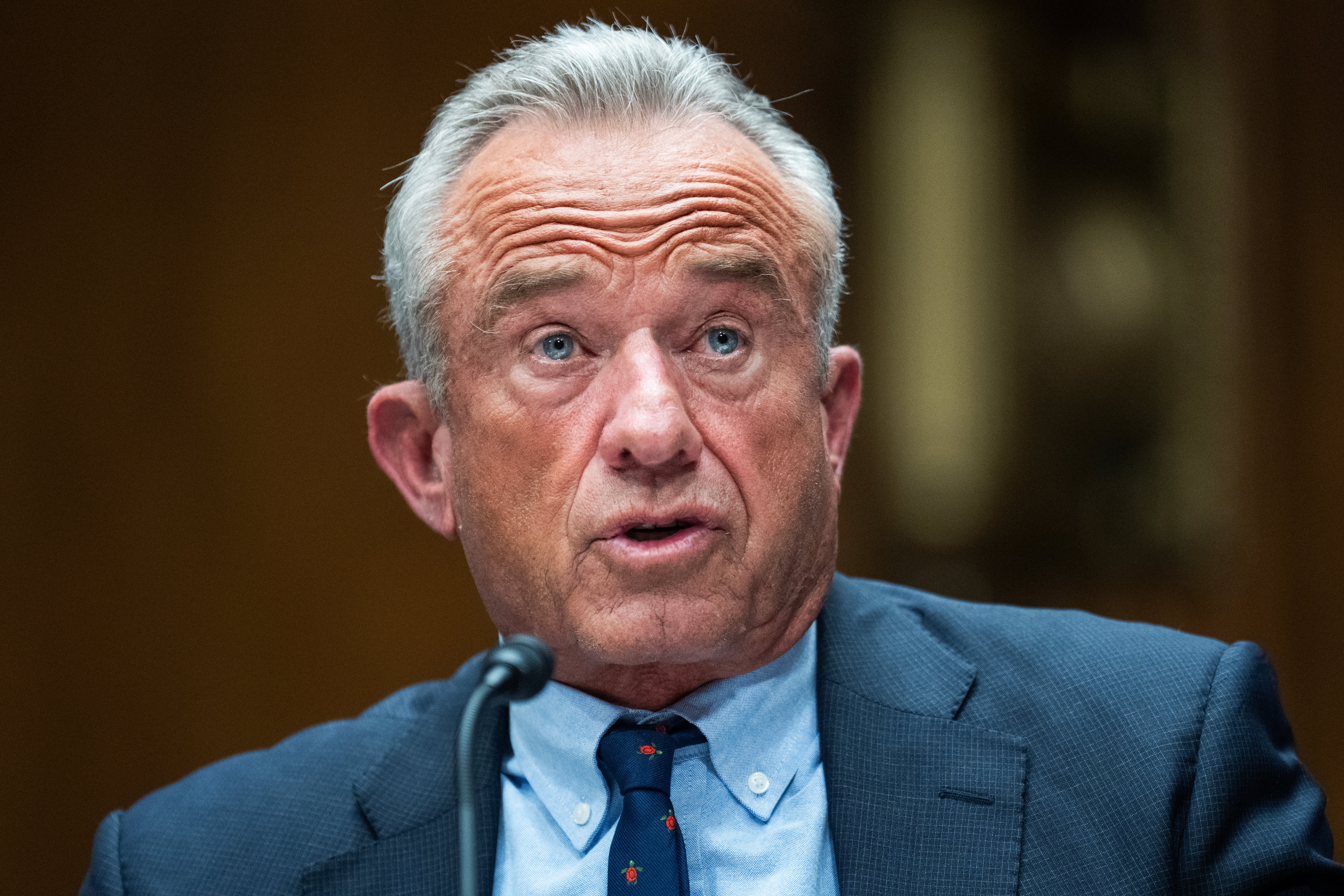 Man speaking into a microphone astatine  an indoor event, wearing a suit   and tie