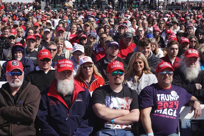 A ample  assemblage  of people, galore  wearing reddish  hats, seated outdoors astatine  a nationalist   event, focusing attentively toward the front