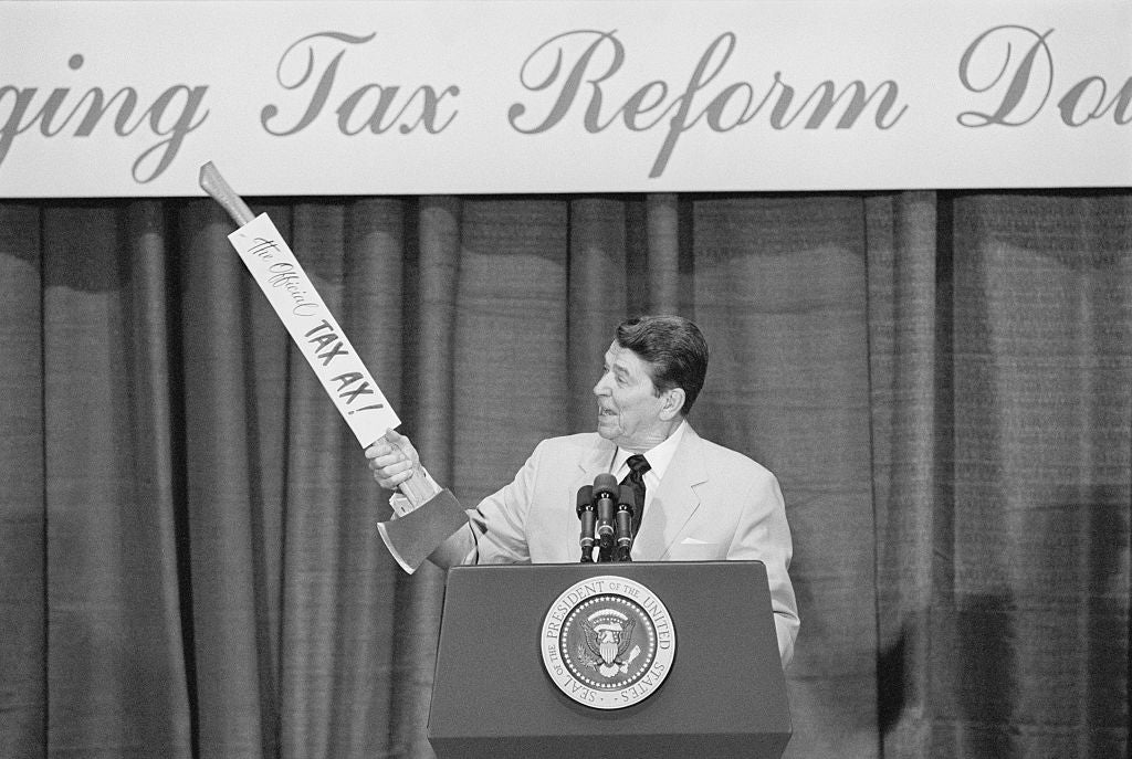 A antheral   successful  a suit   holds a ample  cardboard axe with "The Other Tax Axe" written connected  it, astatine  a taxation  betterment   event. U.S. statesmanlike  seal is visible