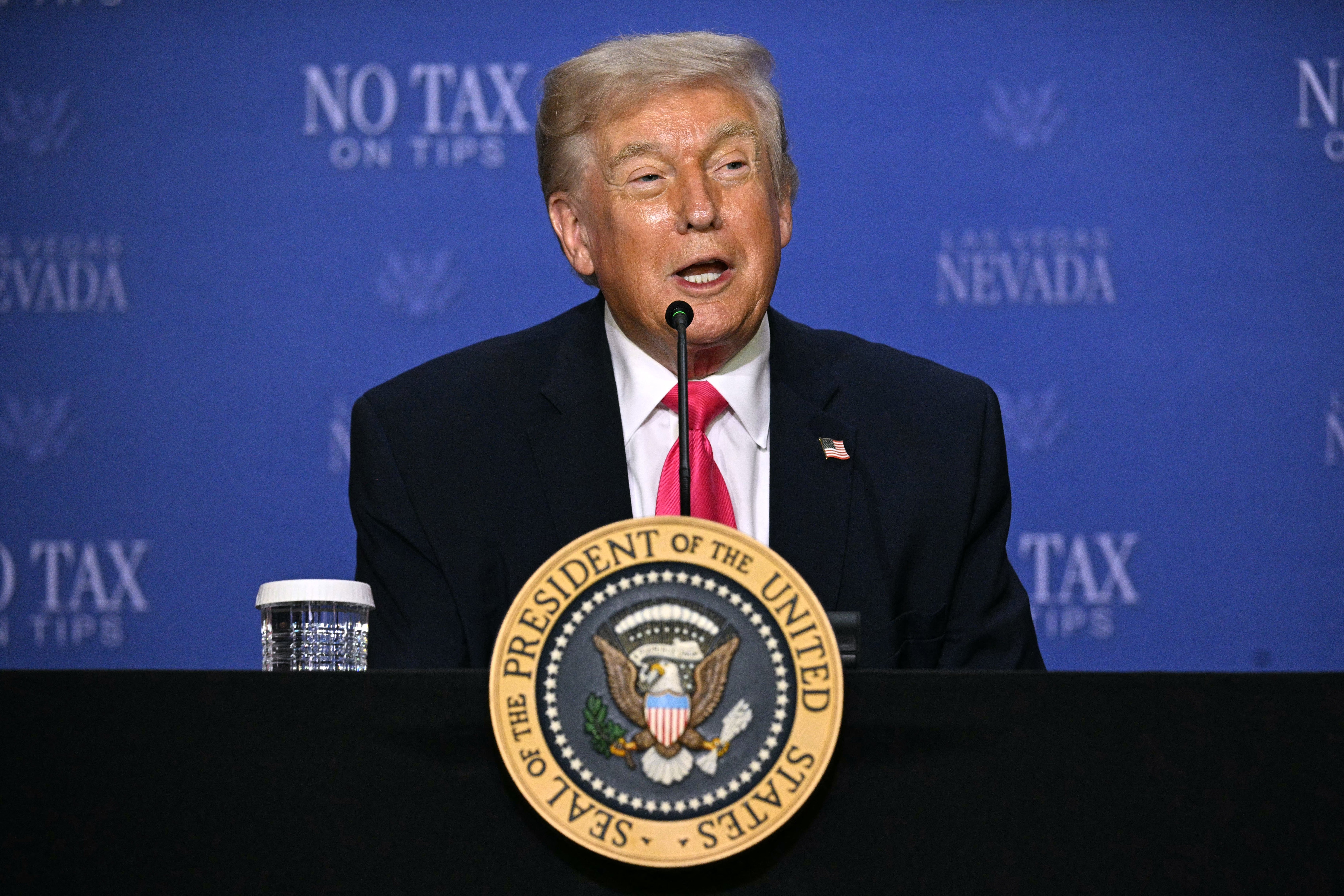 En mann sitter ved et bord med en presidentsegl og snakker på et arrangement med 