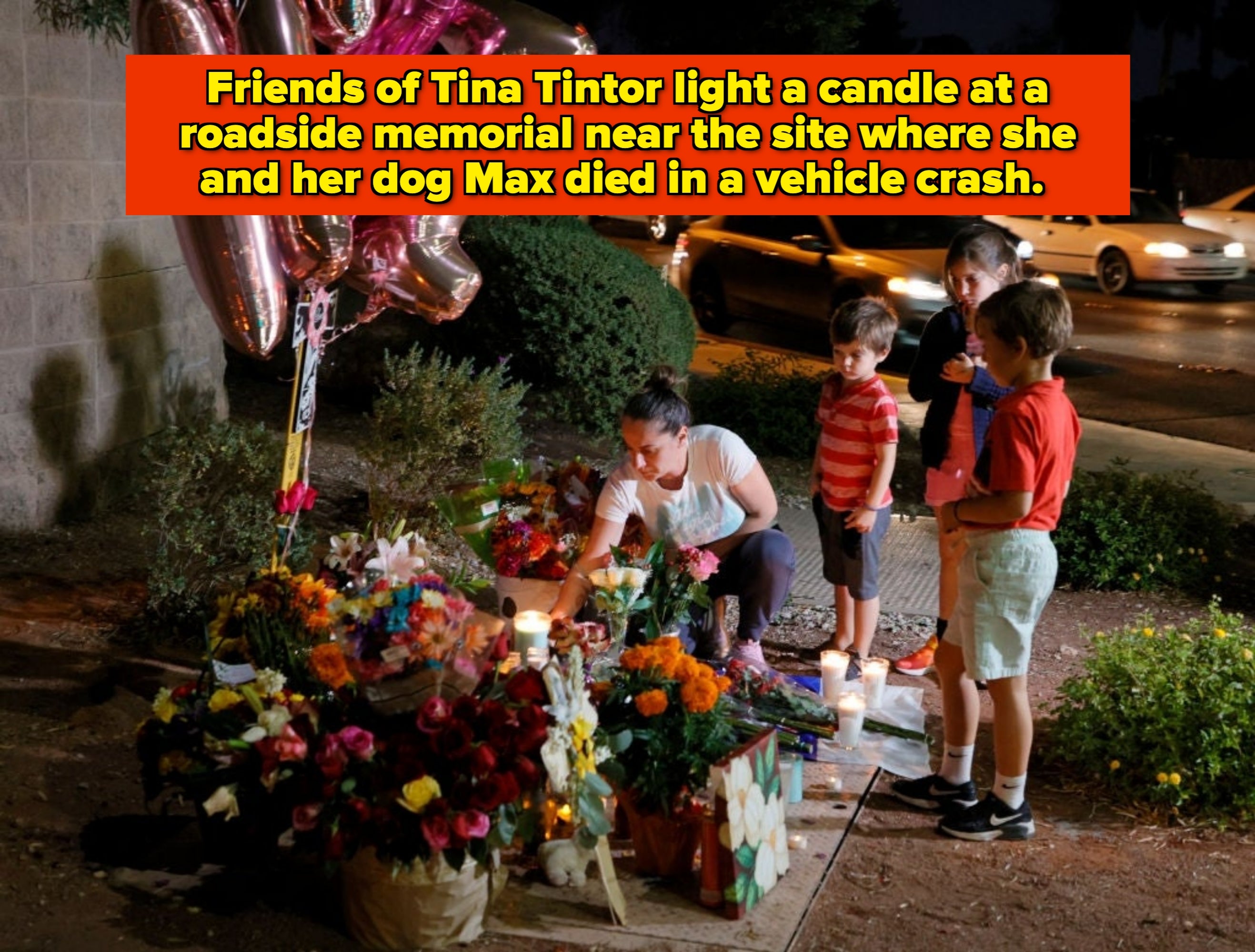 A pistillate   and 3  children spot  flowers and candles astatine  a roadside memorial astatine  night