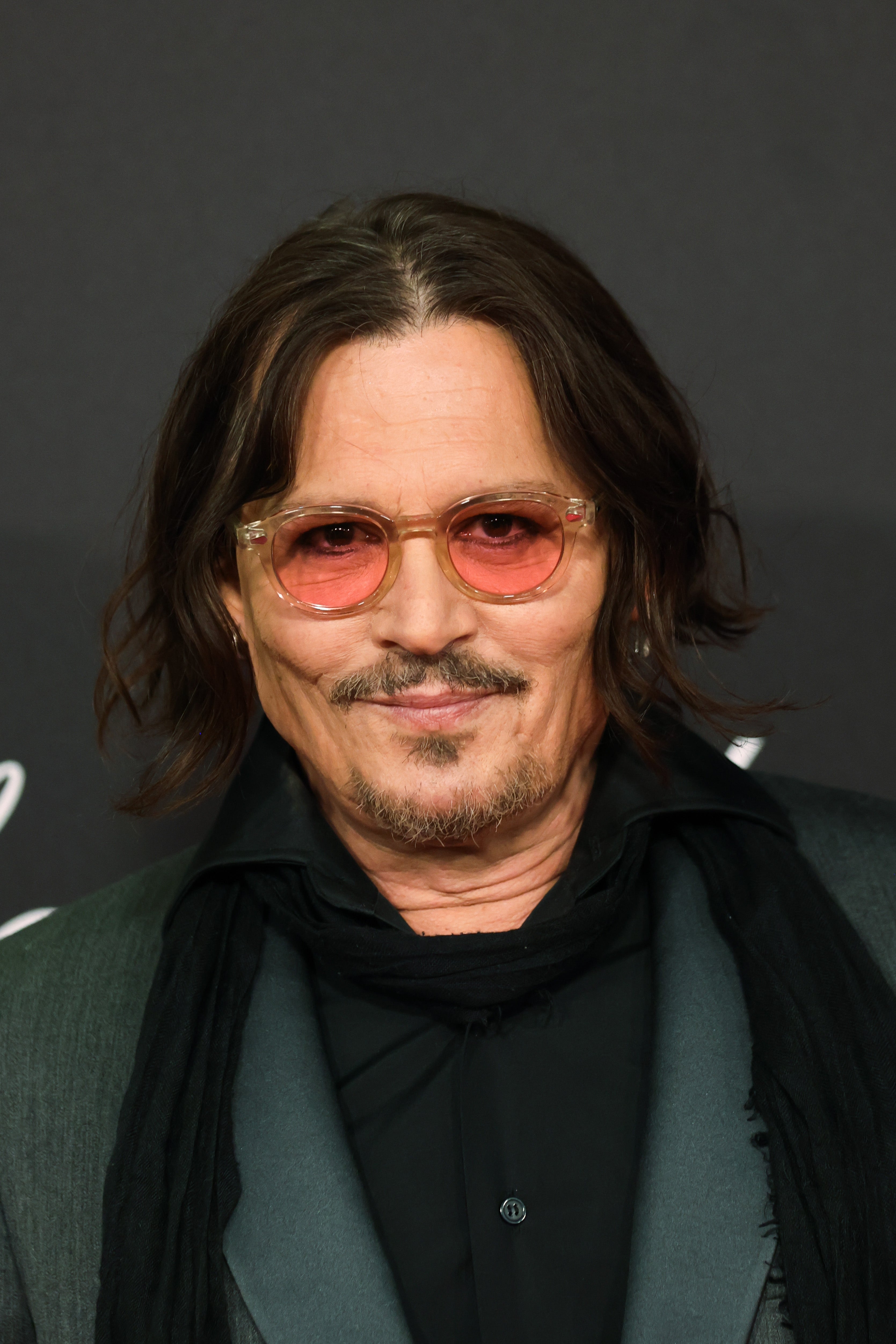 Johnny Depp wearing tinted glasses and a suit   with a scarf, smiling astatine  an event
