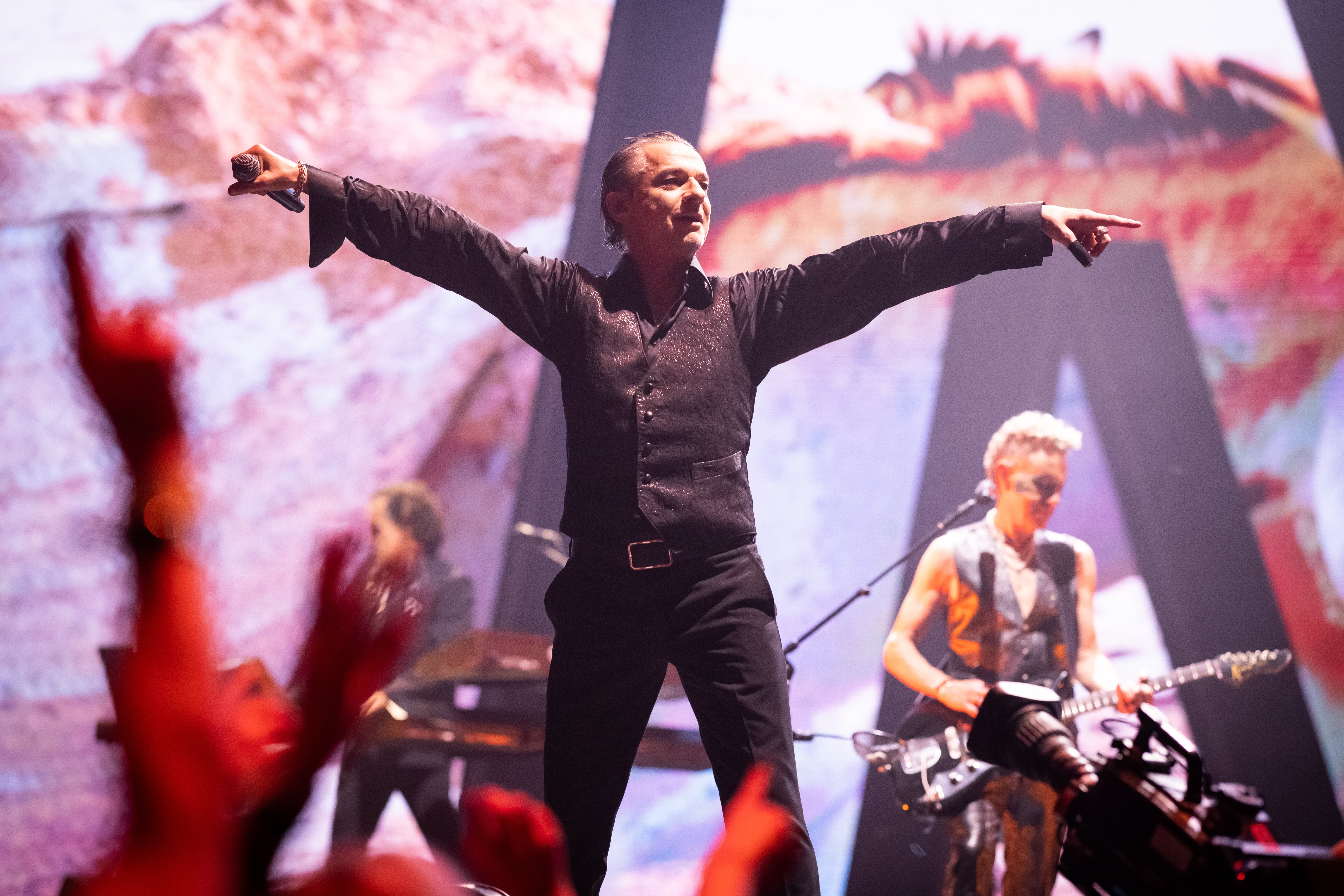 Performer connected  signifier    holding a mic, arms outstretched. Band plays successful  inheritance  with dynamic lighting and an energetic crowd