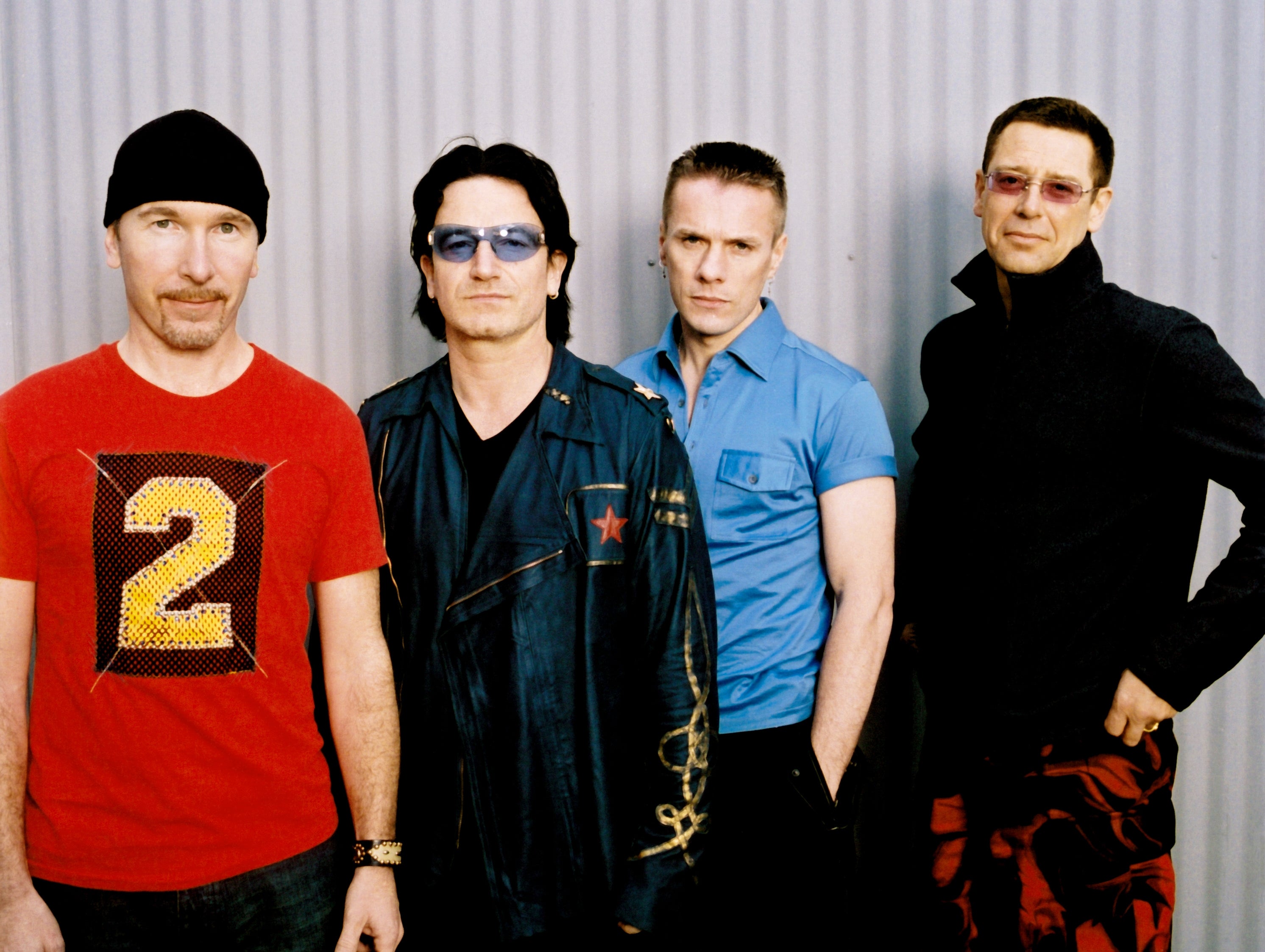Four men posing casually successful  stylish outfits against a corrugated backdrop, featuring leather jackets and a premix  of relaxed and ceremonial  attire