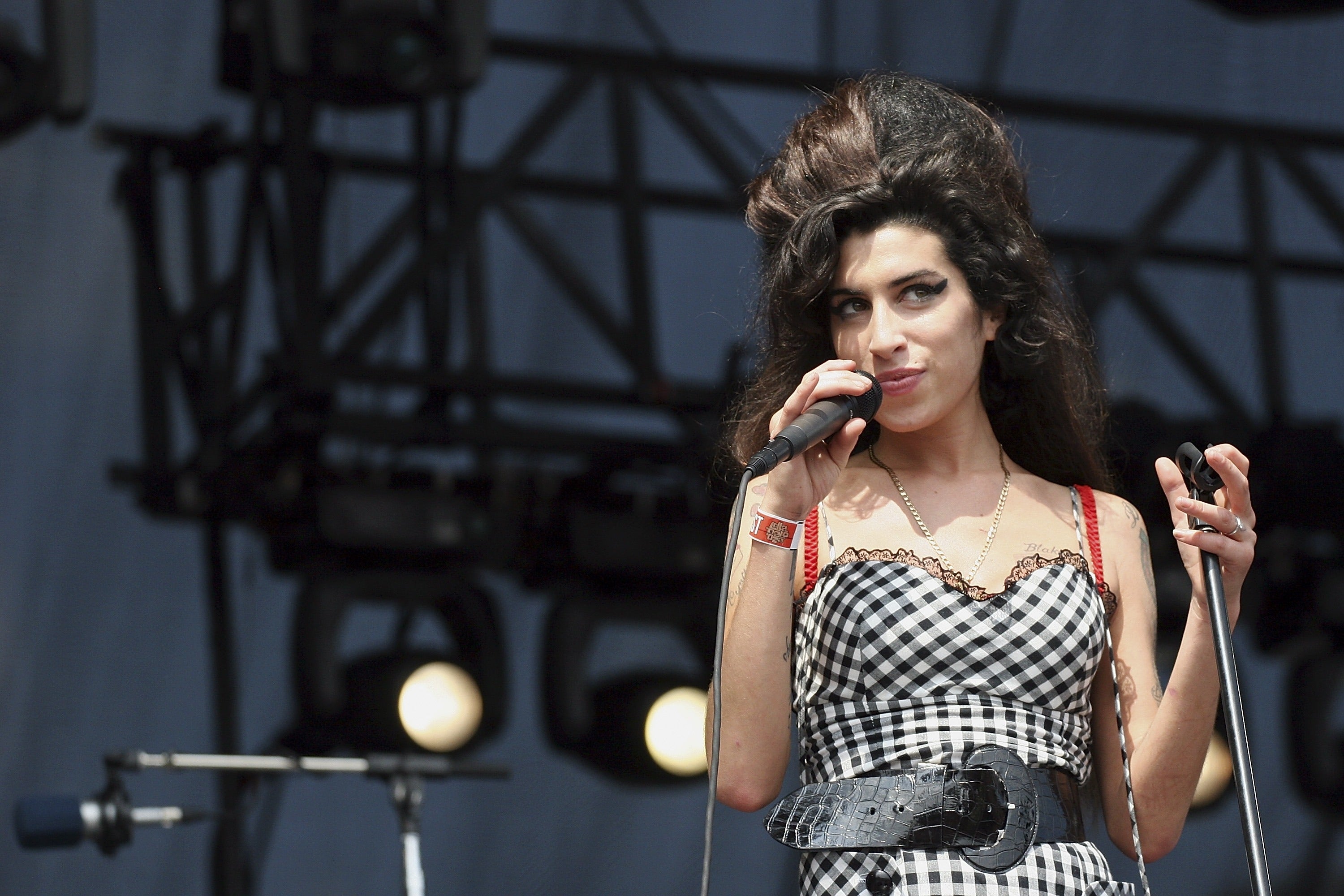 Singer performs connected  signifier    wearing a checkered formal  and wide   belt, holding a microphone. Hair styled successful  a voluminous beehive