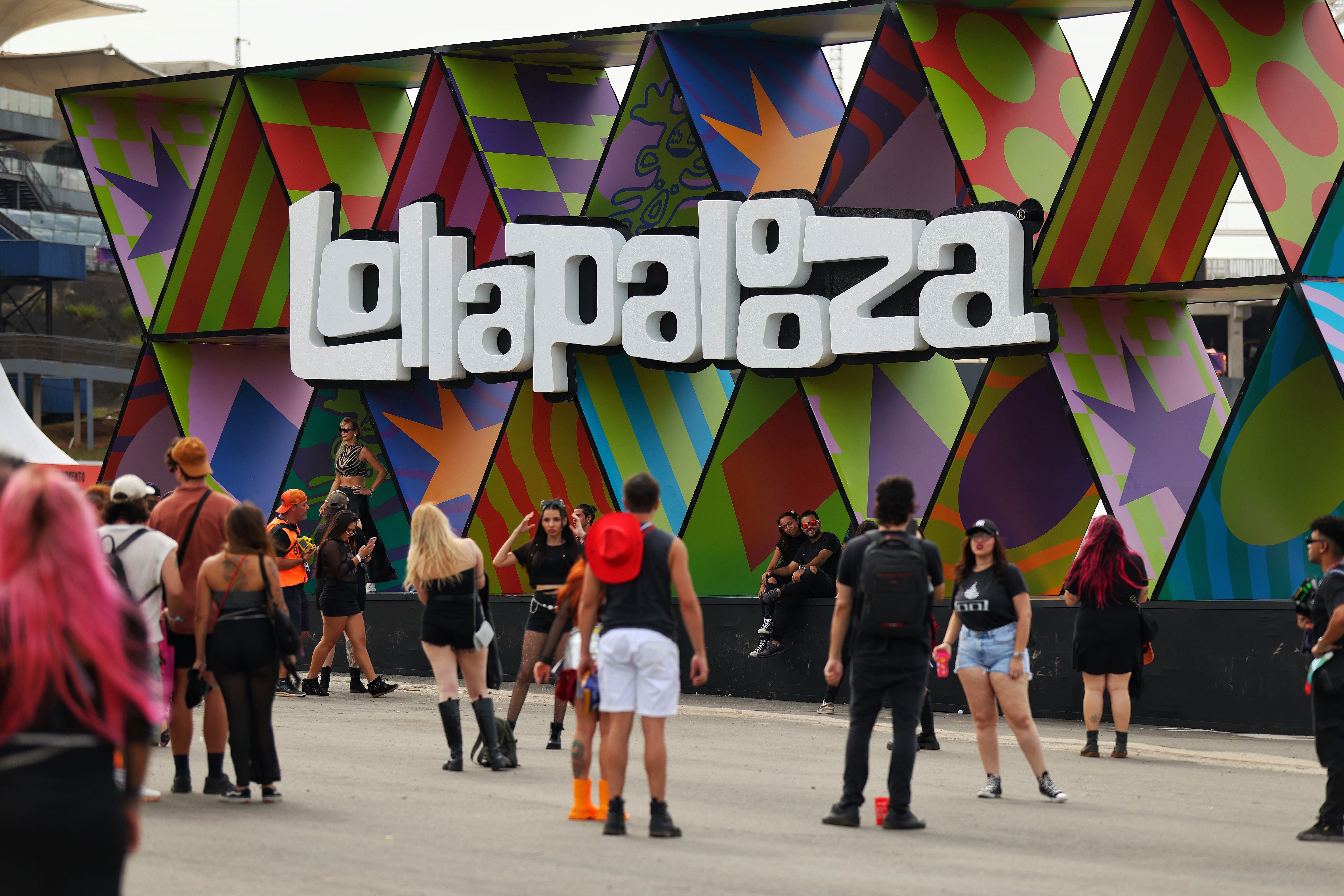 People stitchery  adjacent   the colorful Lollapalooza festival entrance, wearing casual summertime  outfits