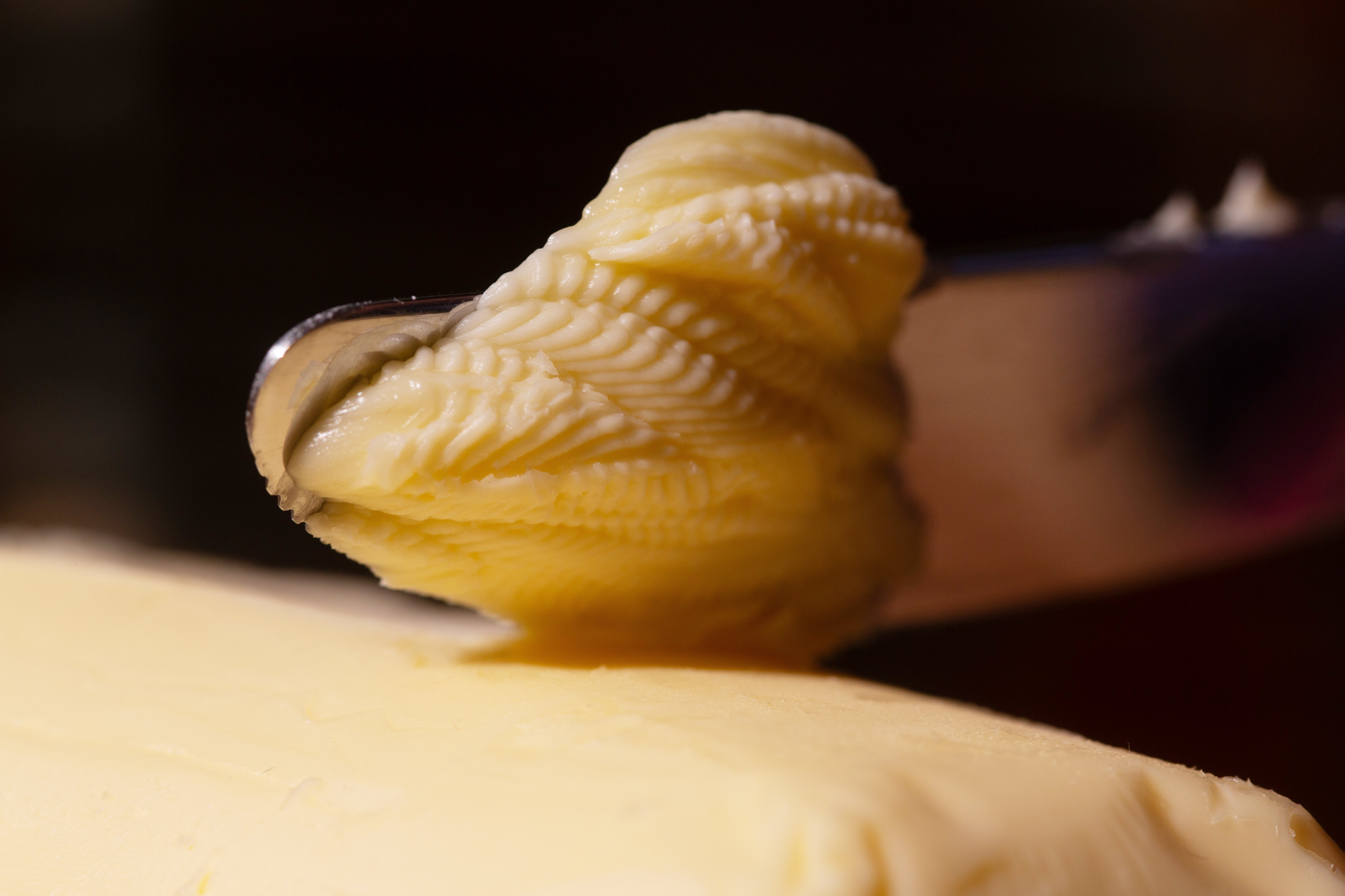 Butter being dispersed  onto a aboveground  with a knife, capturing the texture and item  of the butter
