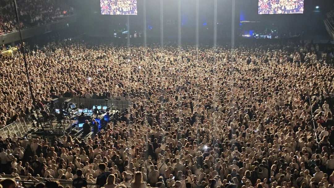 Large assemblage  astatine  a packed performance  venue, signifier    lights illuminating the audience, with large  screens displaying visuals above