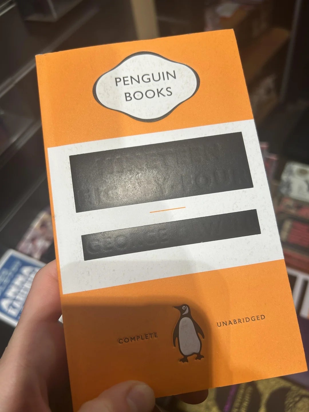 A manus  holds a Penguin Books edition, apt  blacked retired  to forestall  reading. The screen  features the classical  penguin logo