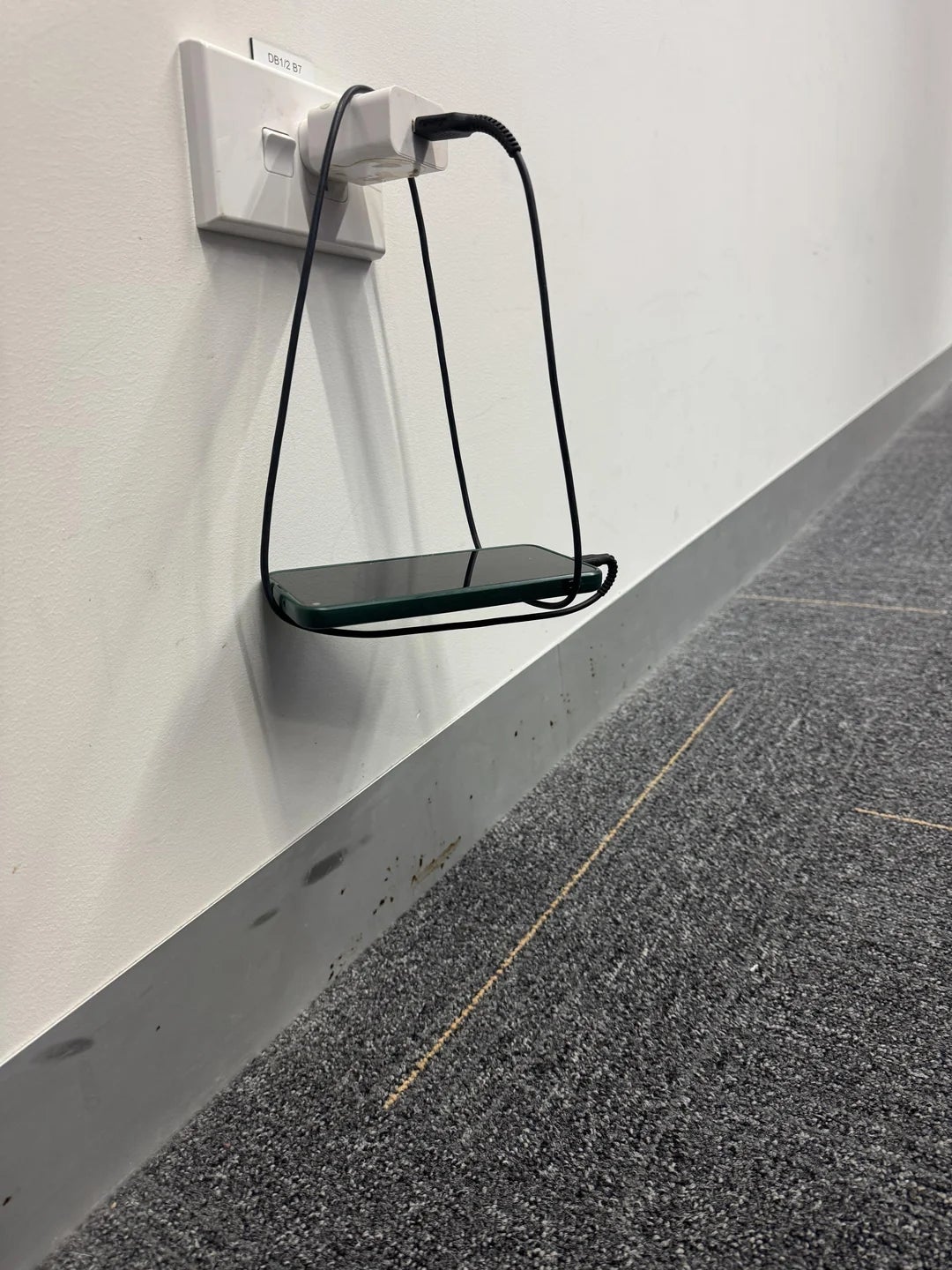 Smartphone placed connected  a solid  shelf, charging from a partition  outlet