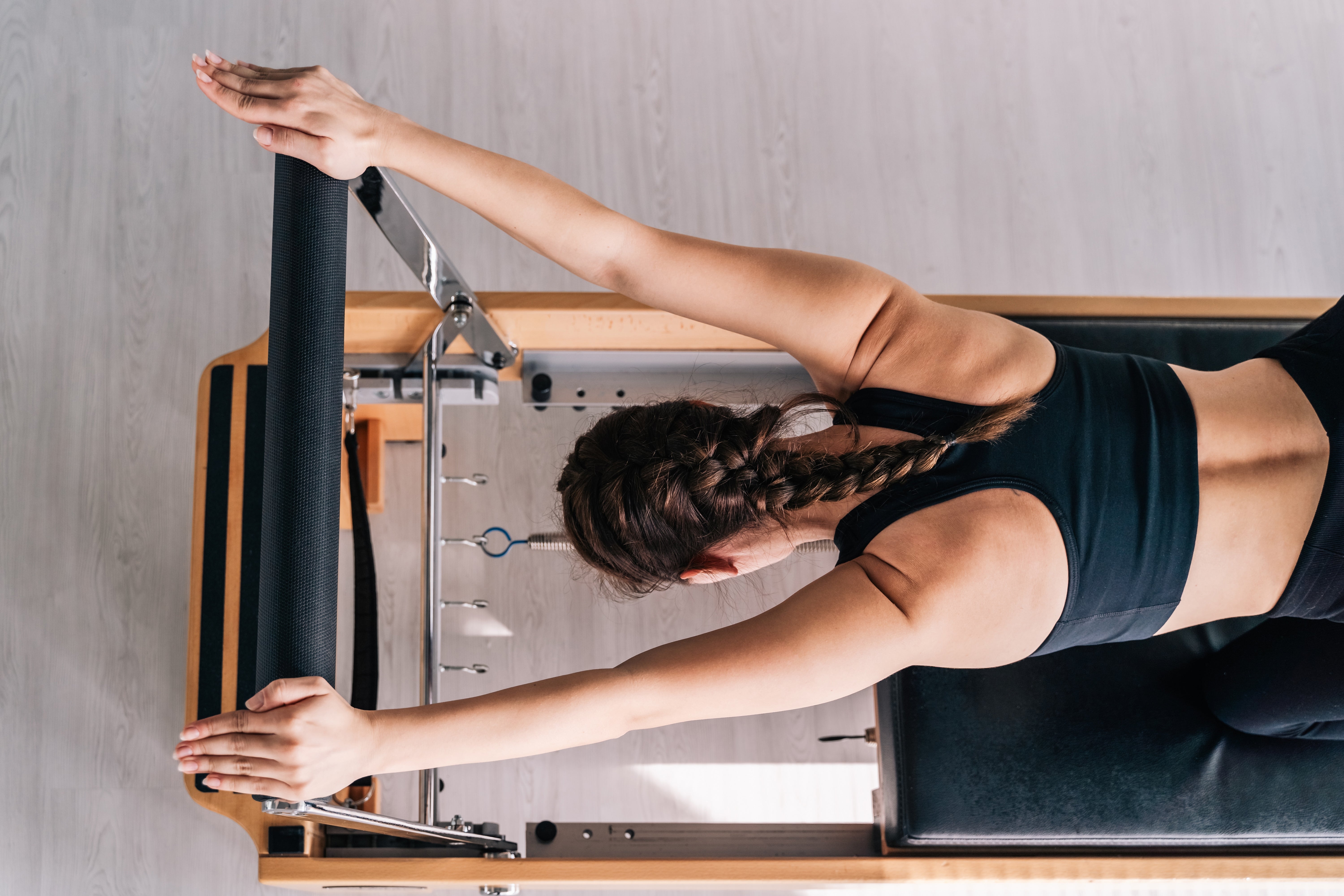 Person med en flette som utfører øvelser på en Pilates reformer-maskin, iført en ermeløs topp og atletiske bukser