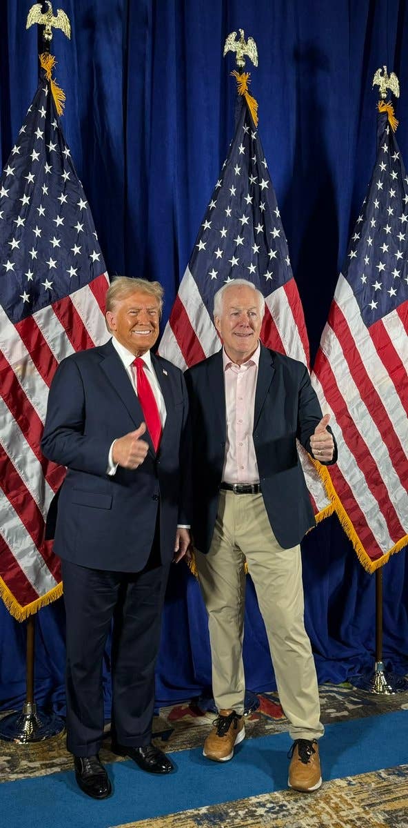 Two men are lasting  smiling with thumbs up   successful  beforehand   of flags. The antheral   connected  the near  is wearing a suit   and reddish  tie, the different   successful  a blazer and khakis