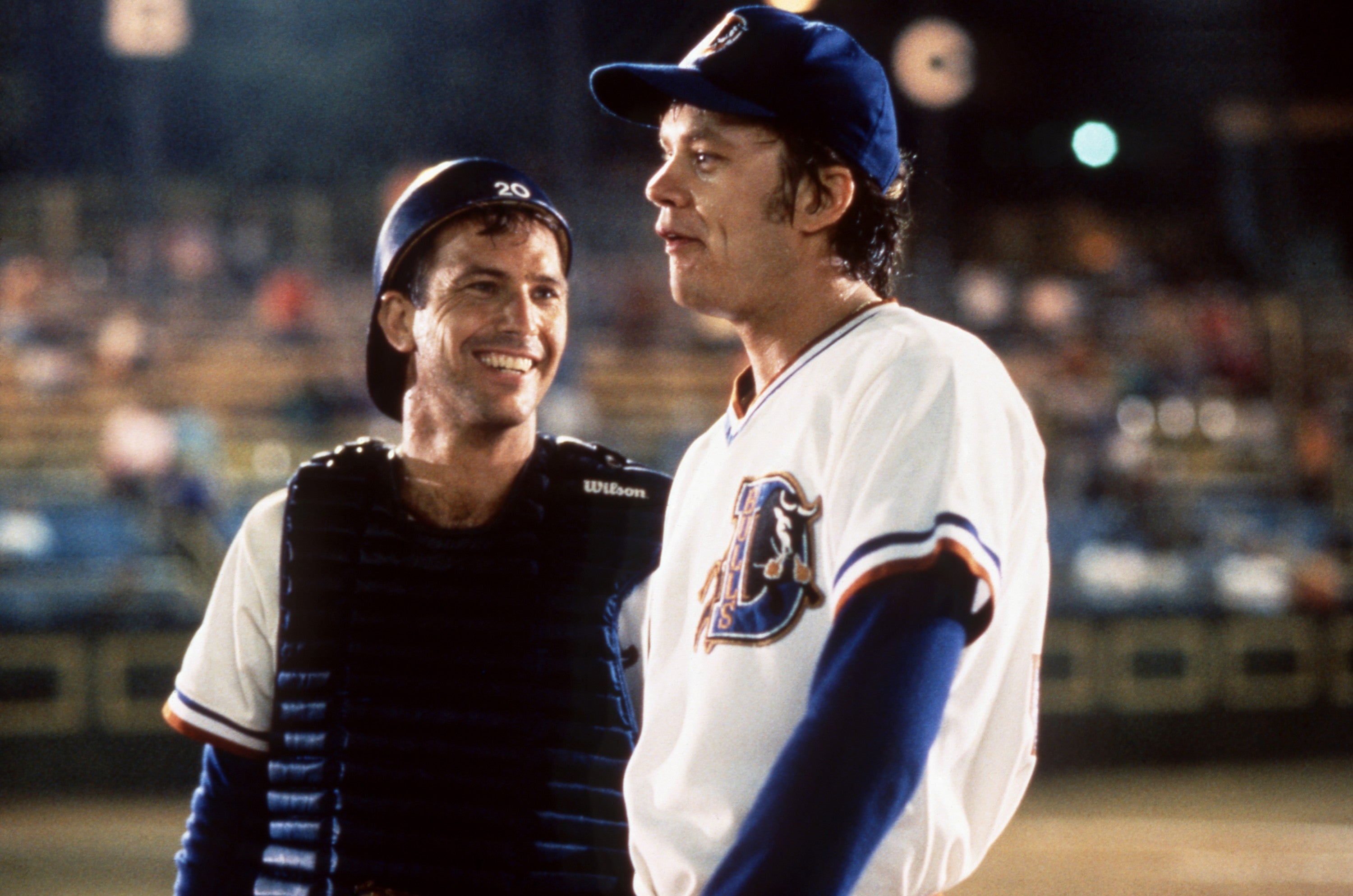 Two baseball players in uniform on the field, one wearing catcher's gear, discussing during a game