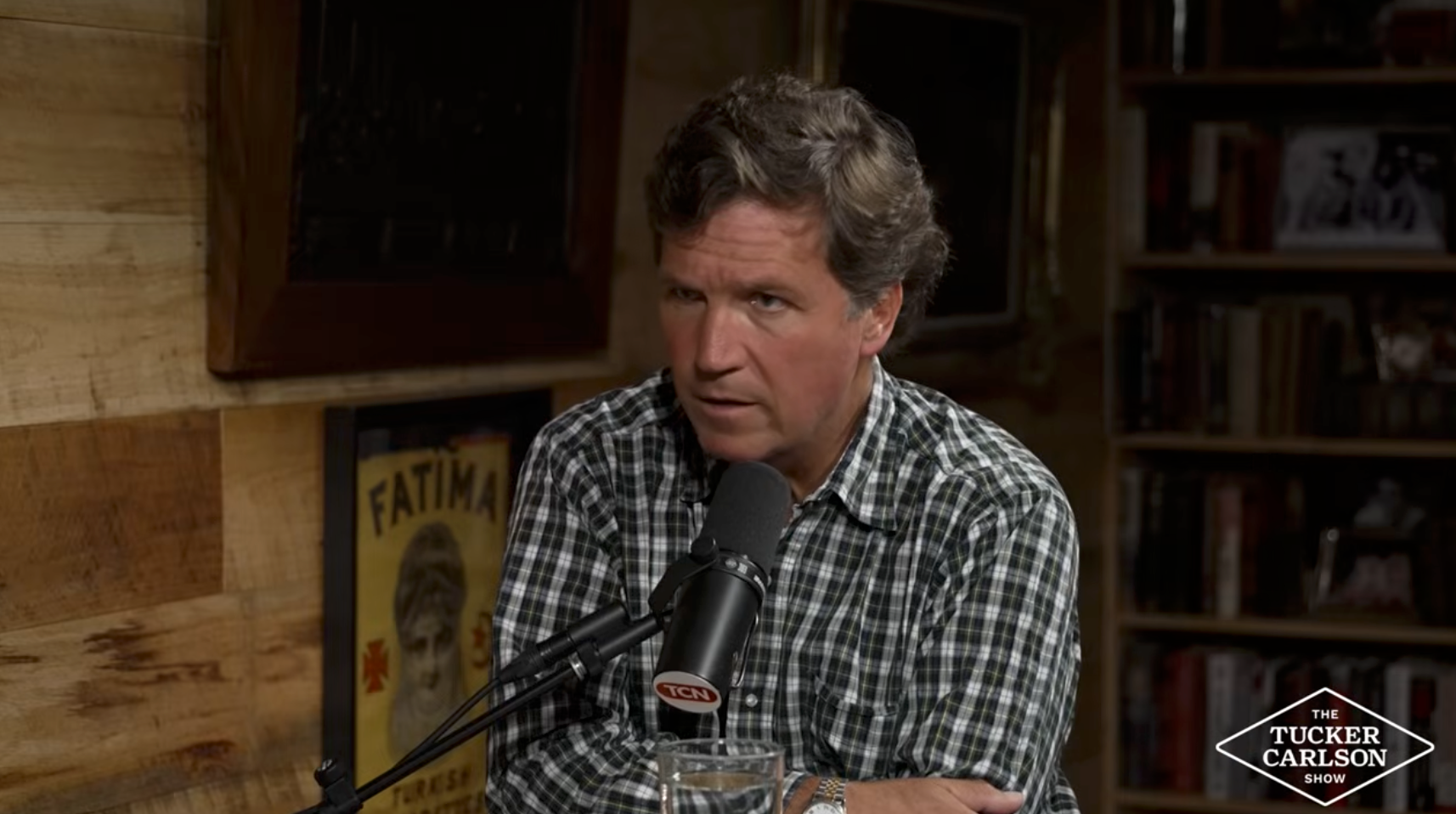 Person i rutete skjorte snakker inn i en mikrofon under et podcastshow. Bøker og plakater i bakgrunnen