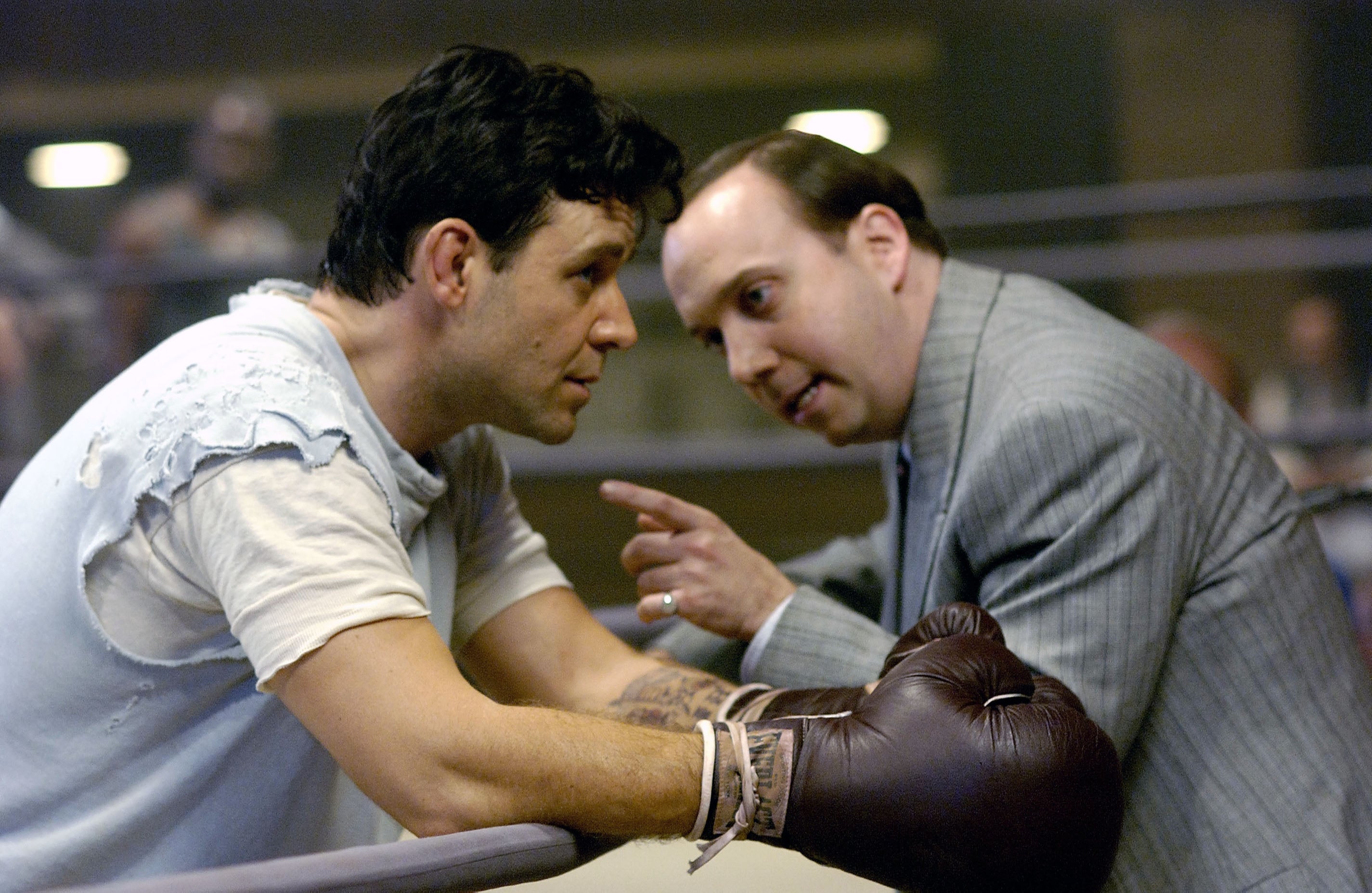 Two men in a boxing ring; one leaning on ropes wearing boxing gloves, the other in a suit, gesturing and speaking intensely