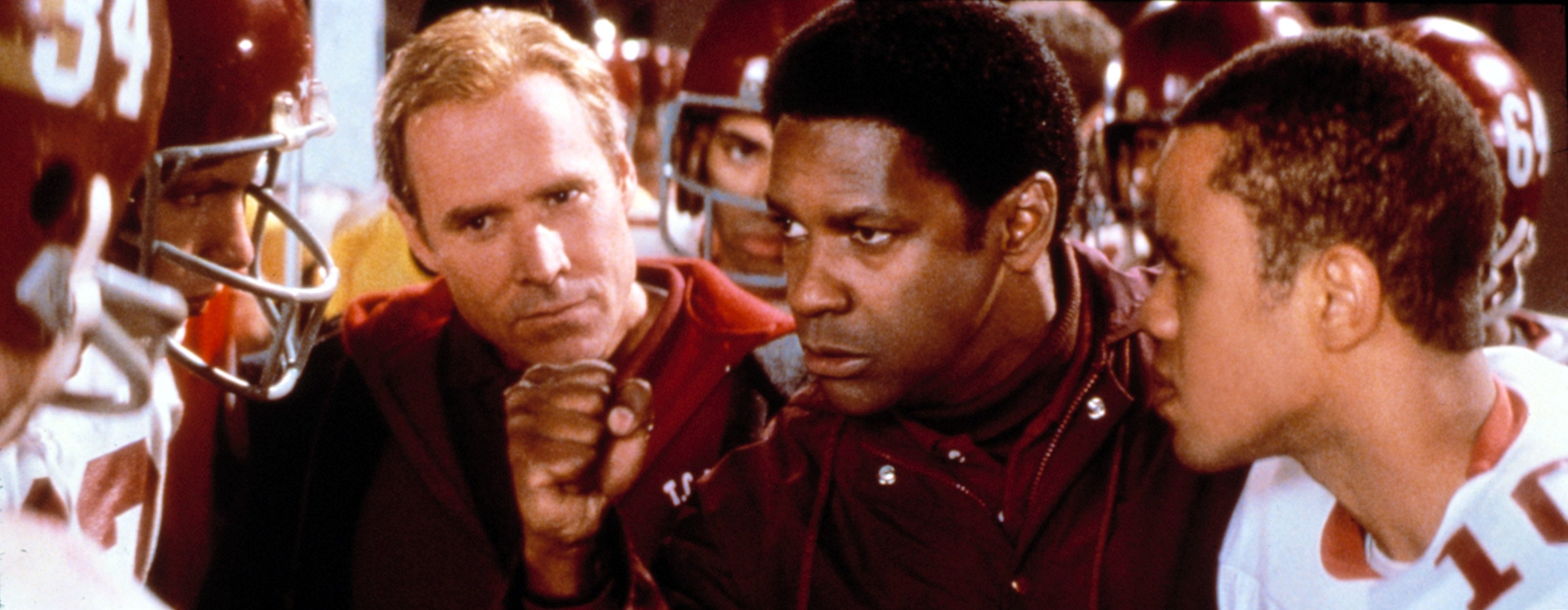Coach motivating a football team on the sidelines, players in helmets listening intently