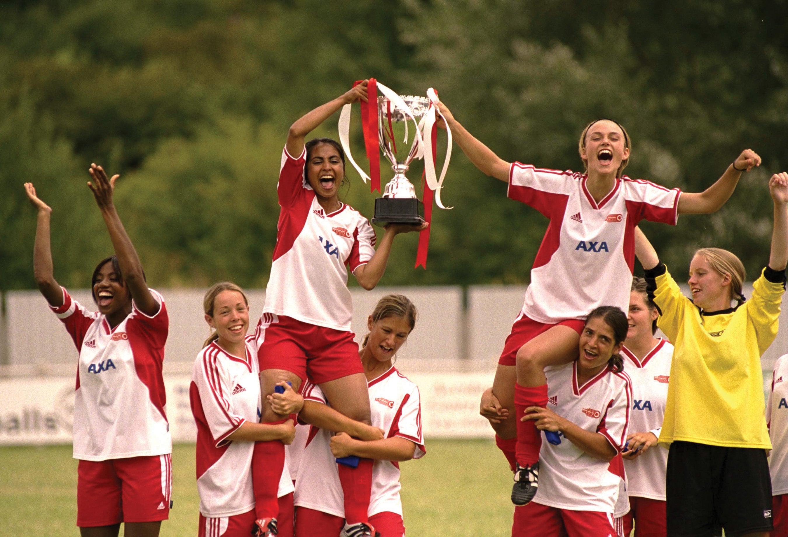 Soccer team celebrating a victory, lifting a trophy with bright expressions, wearing matching jerseys and shorts on a field