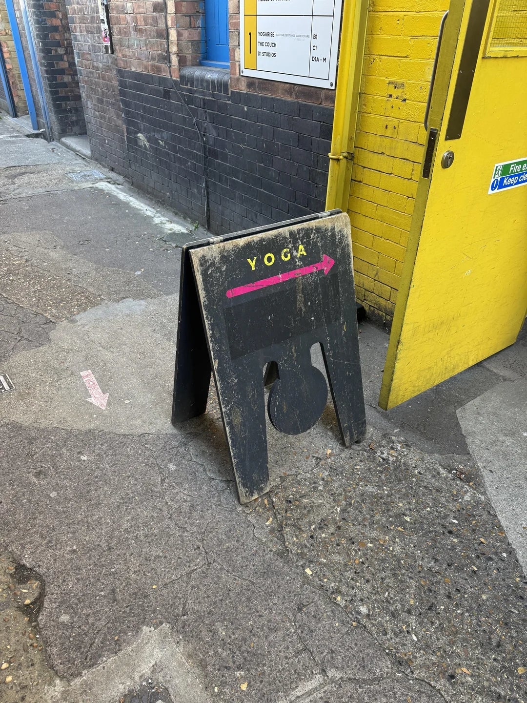 Sign connected  sidewalk with ample  substance   "YOGA" and pinkish  arrow pointing right, placed adjacent   a yellowish  doorway  successful  an municipality  setting