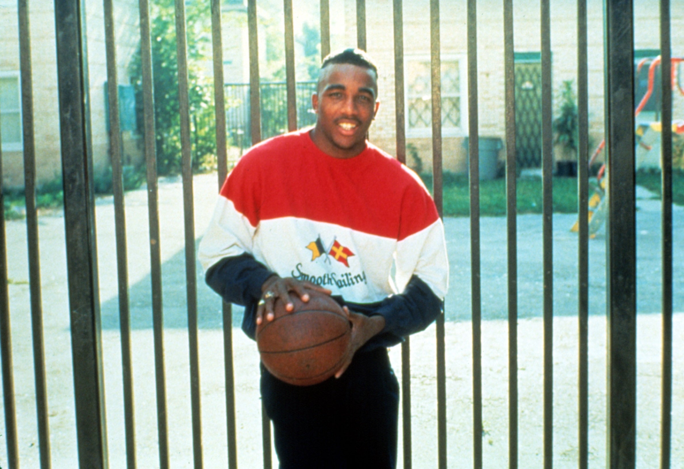 Person in a casual sports sweater holding a basketball, standing in front of a fenced background