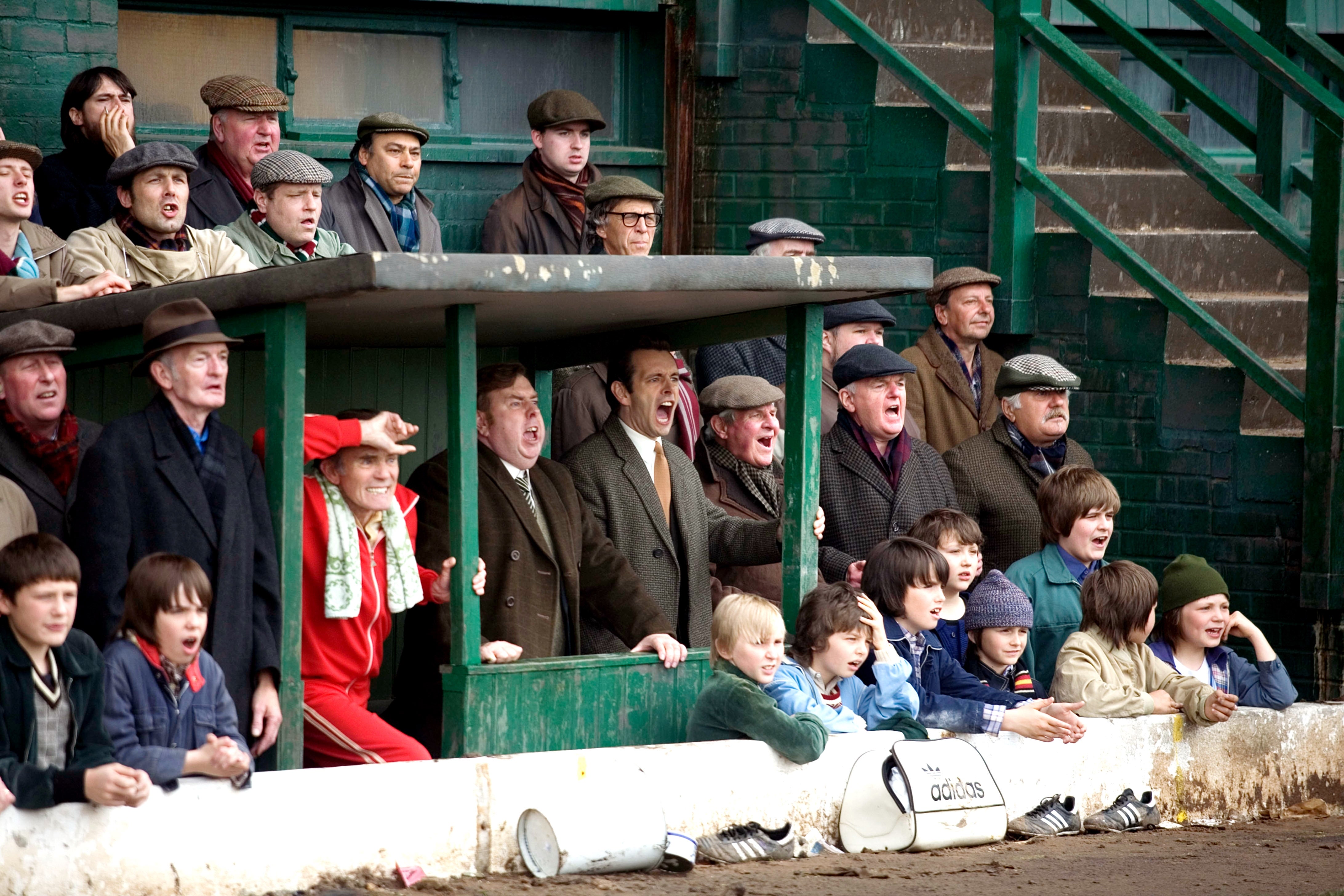 Group of men and children in vintage clothing excitedly watch a sports event from the sidelines