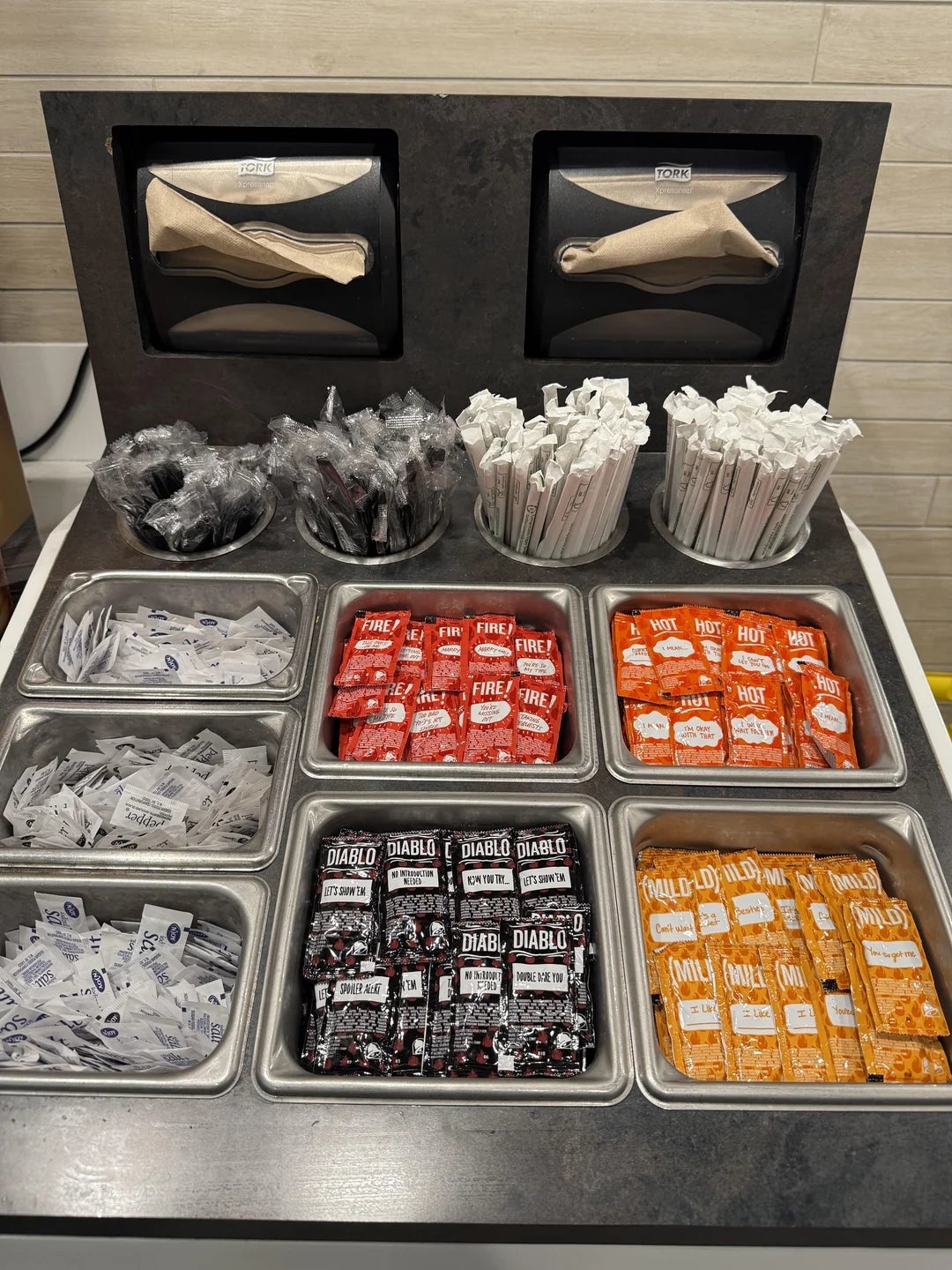 Restaurant condiment presumption    with assorted  blistery  condiment  packets, including Fire, Diablo, Mild, Hot, and Creamy Jalapeño, on  with napkins and utensils