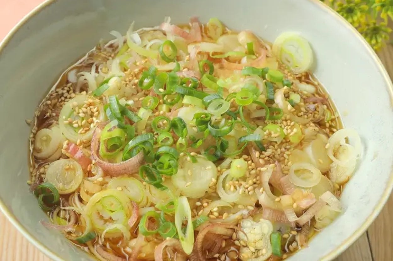 丼に盛られたラーメン。トッピングにはネギとゴマが散らされている。テーブルに花が少し飾られている。