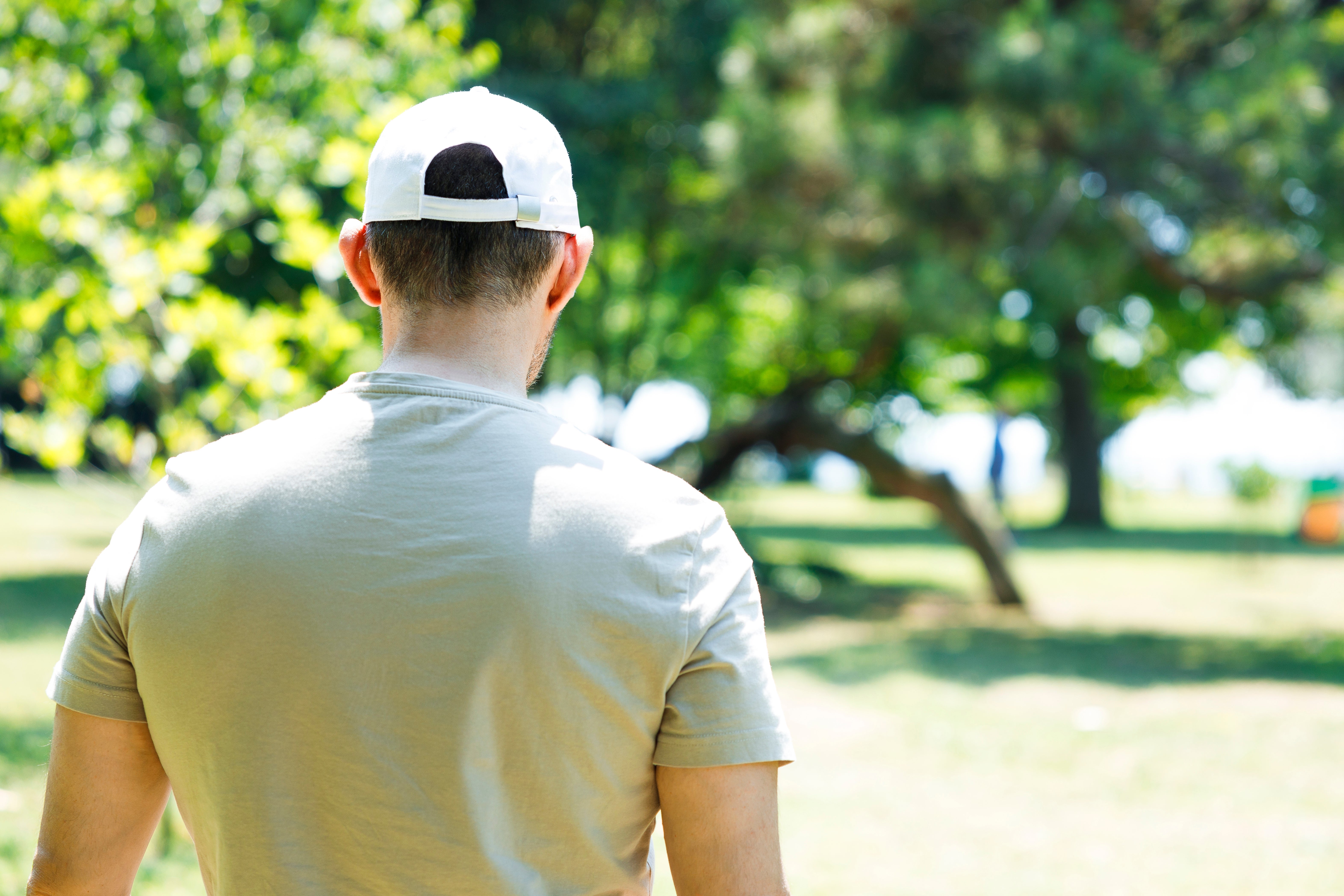 En person i en park sett bakfra, iført en T-skjorte og en caps, nyter en solrik dag utendørs, og foreslår fritid og avslapning