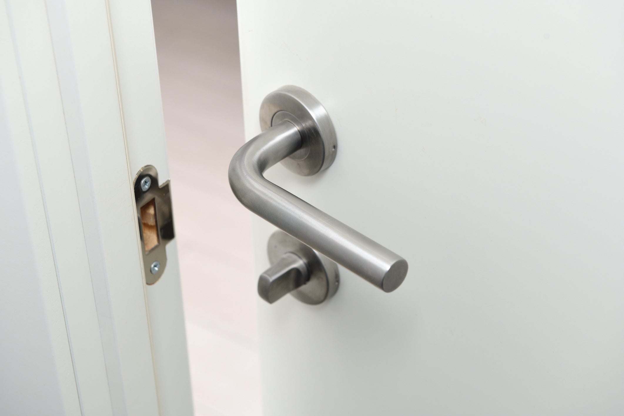 A doorway  somewhat  ajar with a modern   metallic handle, showing portion  of a fastener  mechanism