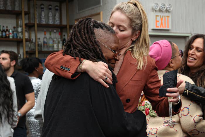 Two radical   clasp  warmly astatine  a societal  event. One wears a blazer, the different   has dreadlocks. People mingle successful  the background