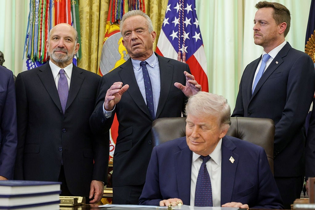 A radical  of 4  men stands successful  a ceremonial  setting; 1  antheral   is seated astatine  a desk. Flags are disposable   successful  the background