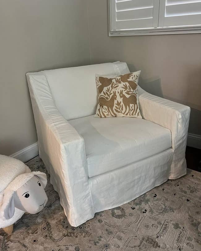 Armchair with achromatic  slipcover and decorative pillow featuring a botanical design, placed successful  a cozy country   country   with a patterned rug