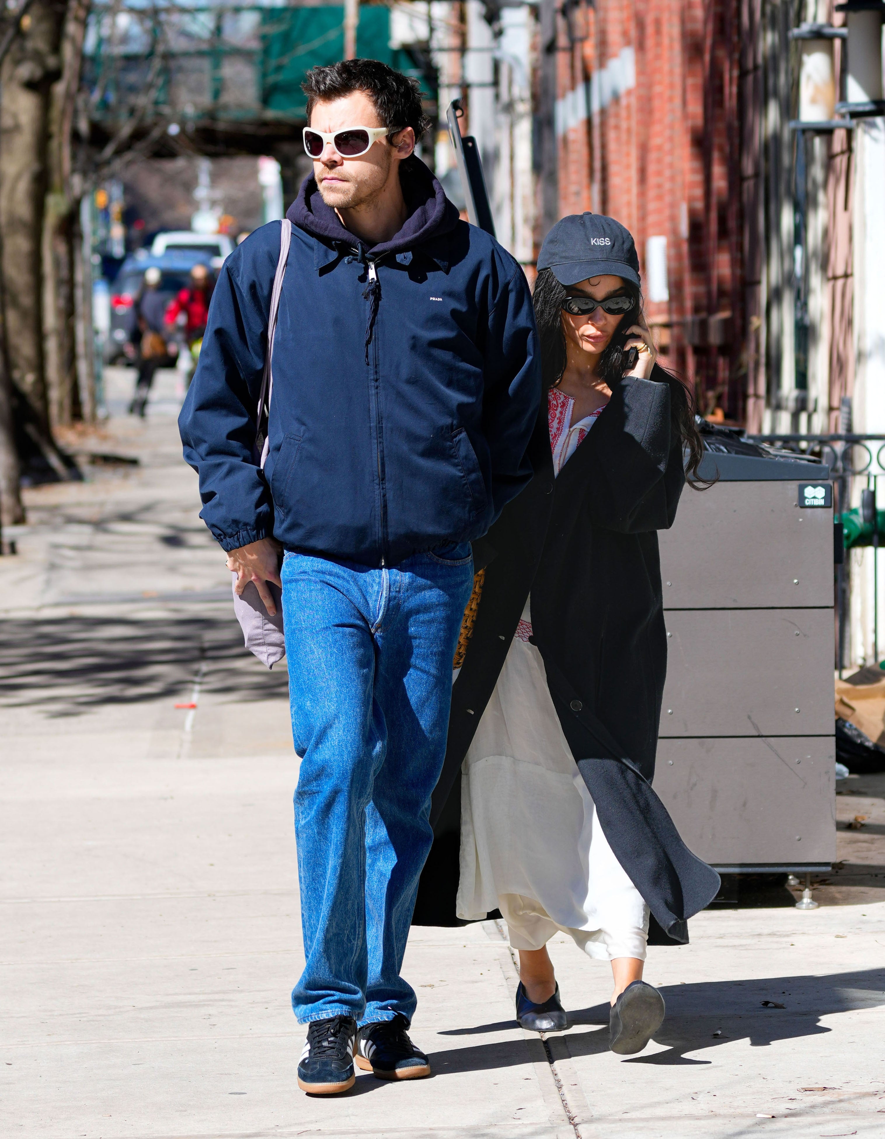 Two people walking outdoors, casually dressed. One wears a navy jacket and jeans, the other in a black coat with a hat